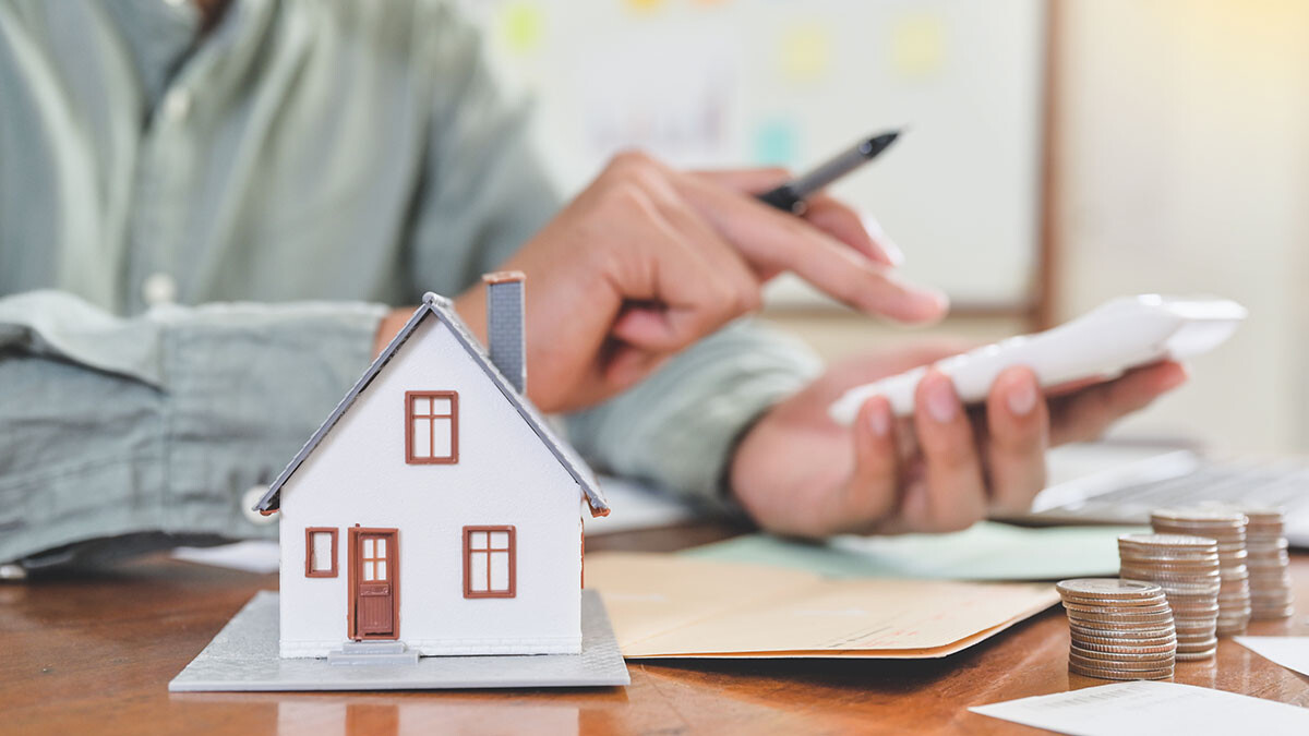 Modell eines Hauses auf dem Tisch, Münzstapel und Person mit Taschenrechner bei Finanzplanung