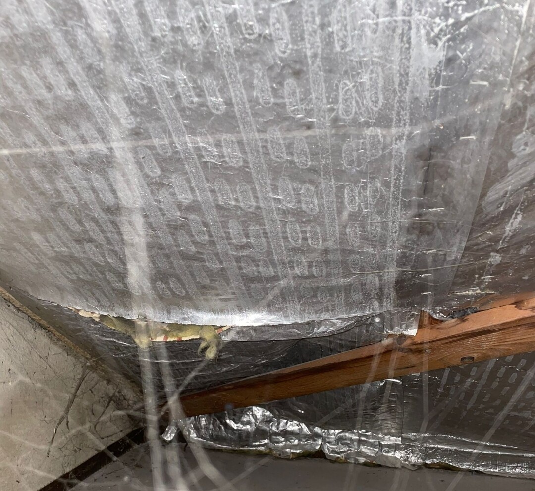 Dachbodenansicht: silberne reflektierende Isolierfolie, Holzbalken und Kunststofffolie.