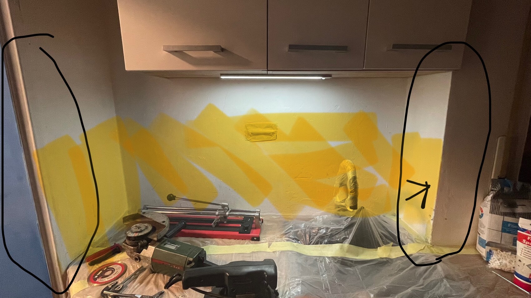 Küchenwand mit gelber geometrischer Malerei, Abdeckfolie und Werkzeugen auf der Arbeitsplatte.
