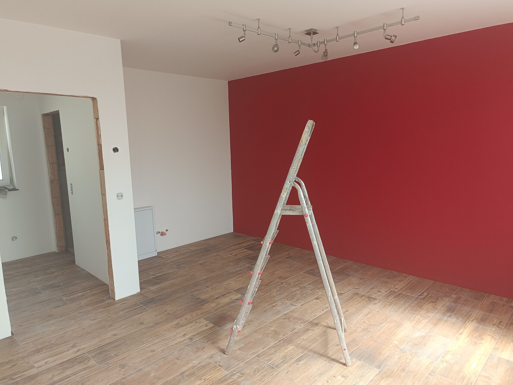 Raum mit roter Wand, eine Leiter steht auf dem Holzboden, Renovierungsarbeiten.