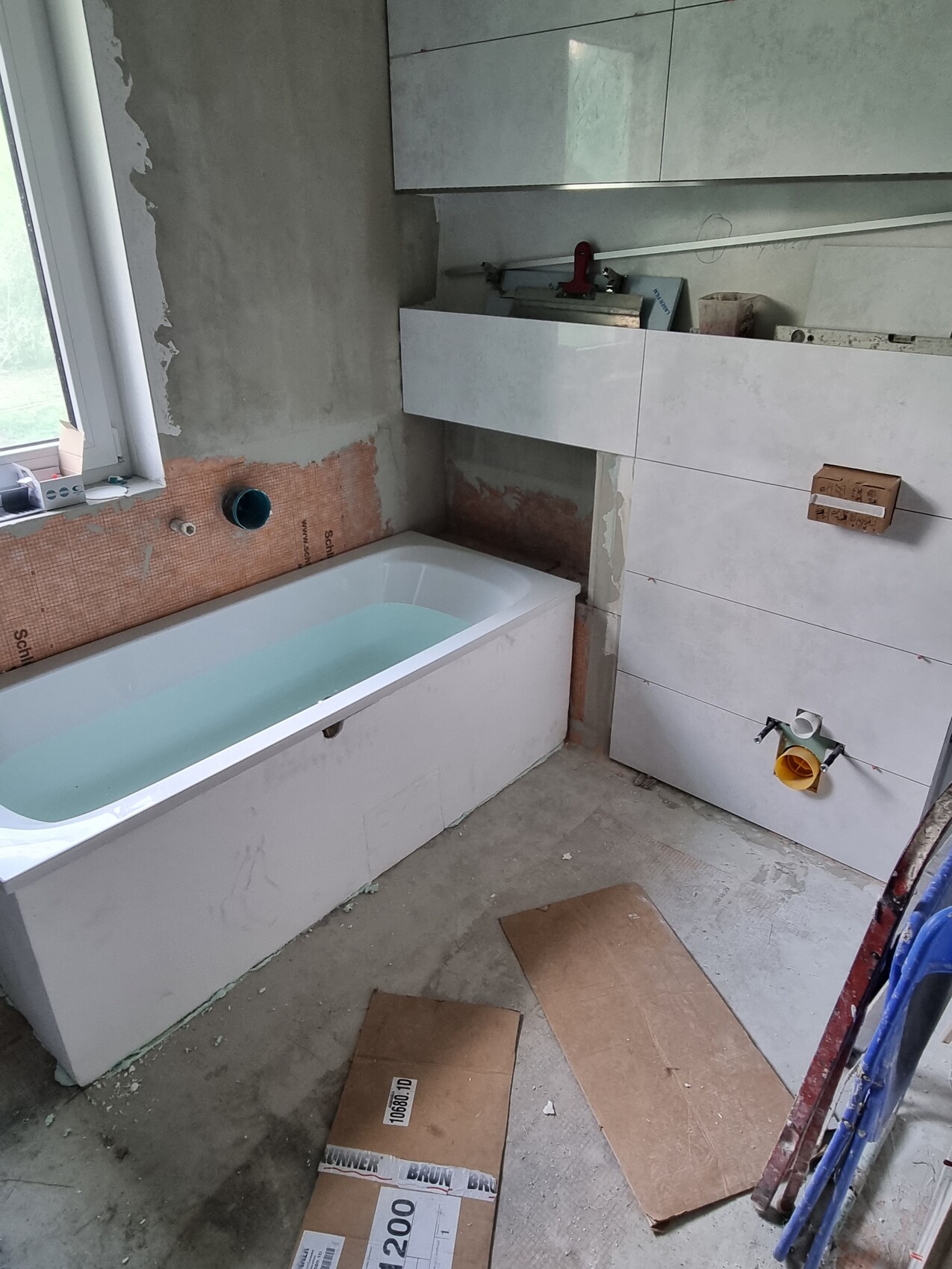 Badezimmer-Renovierung: Badewanne, Fliesenarbeiten, Werkzeuge, Kartons auf dem Boden.