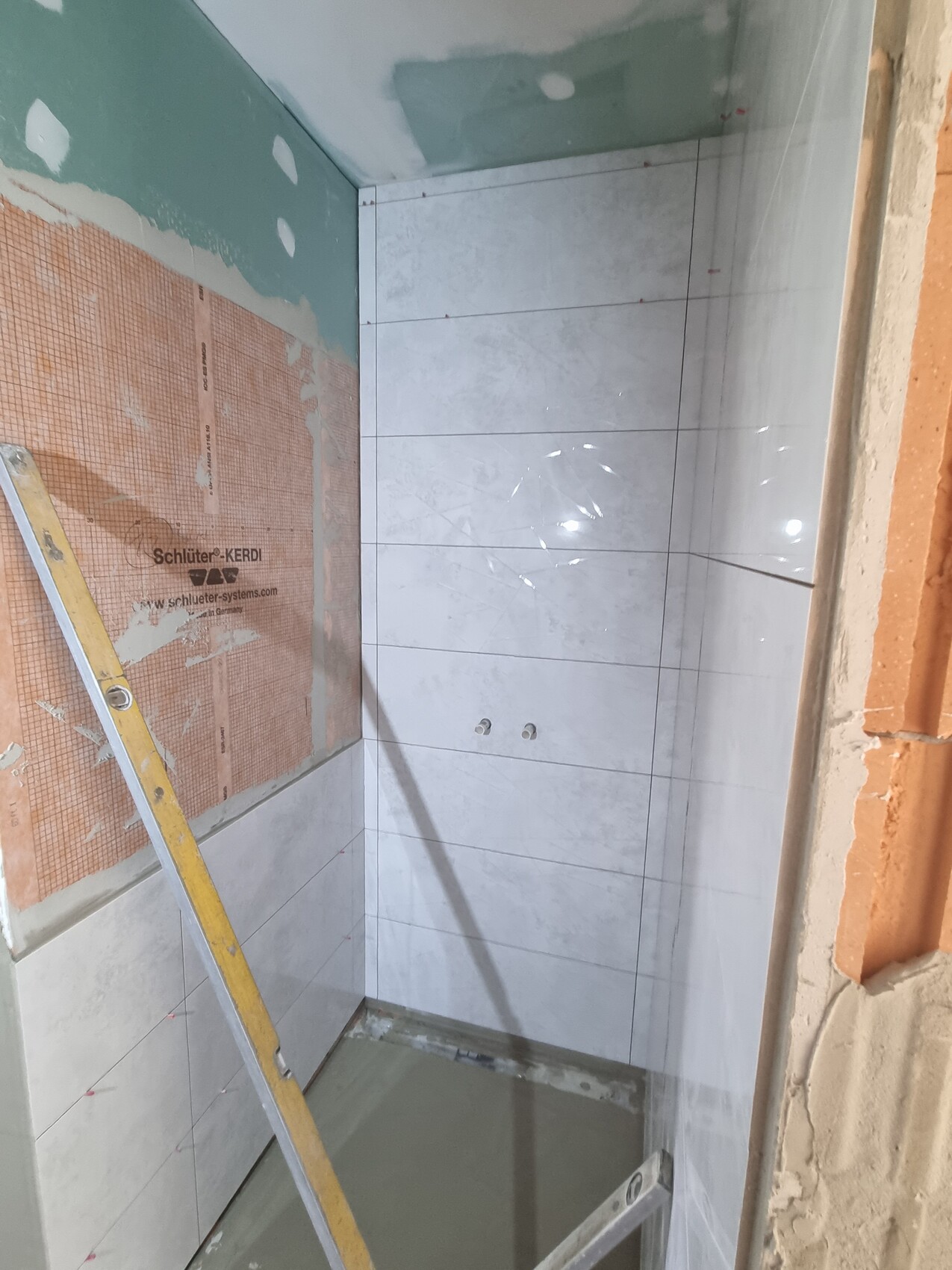 Badezimmer im Bau: Wände teils gefliest, Leiter steht, links Schluter-KERDI sichtbar.