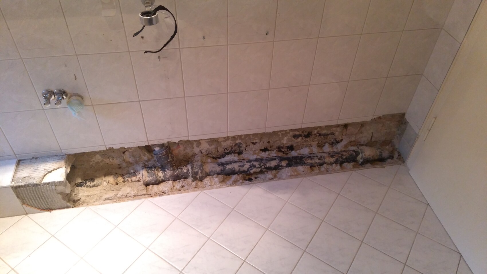 Freigelegter Rohrkanal in einer Badezimmerwand; offene Rohre, Zement und Mauerwerk sichtbar.