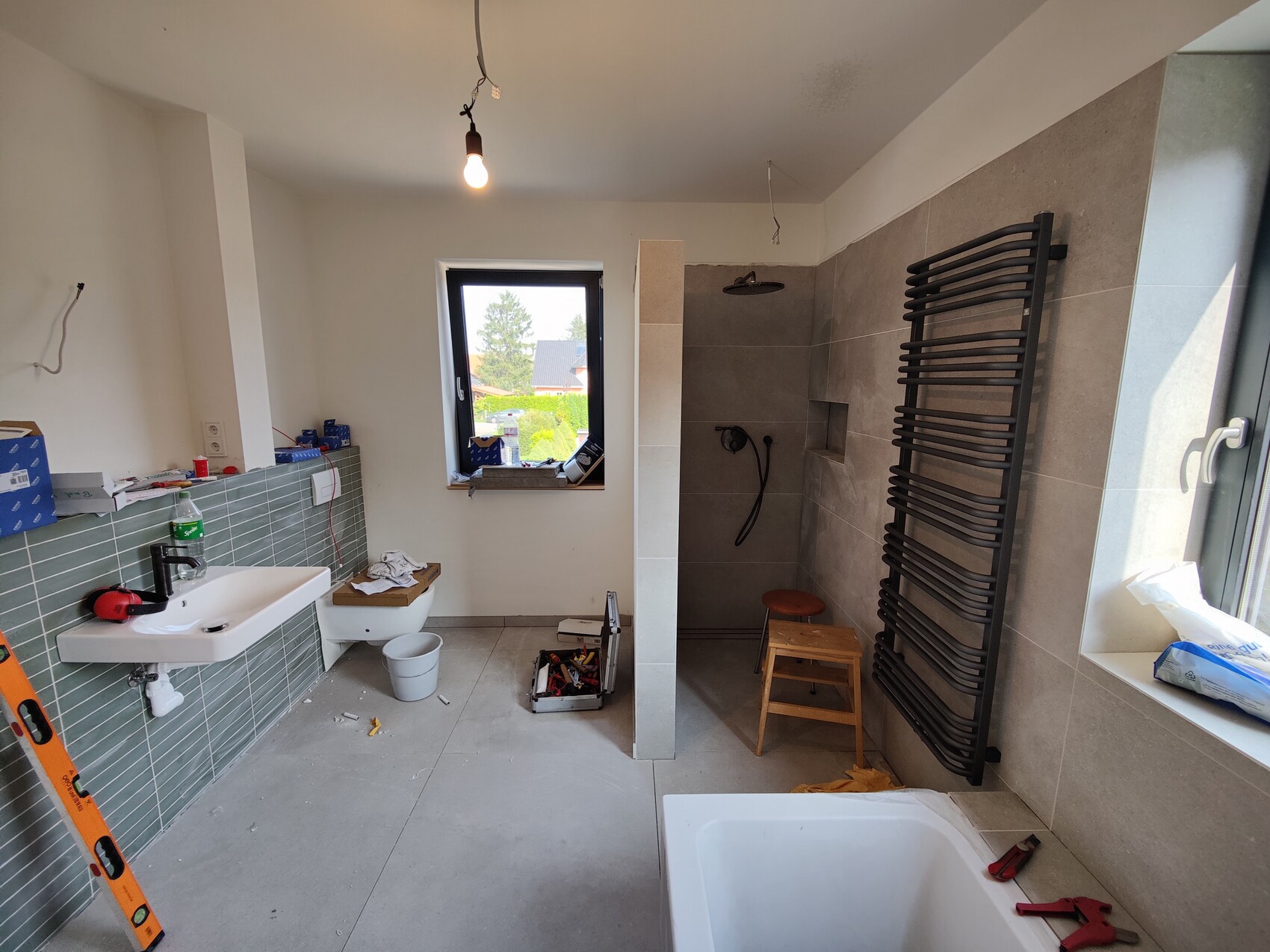 Badezimmer im Bau: Waschbecken, Toilette, Dusche, Heizkörper, Baumaterialien und Werkzeuge.