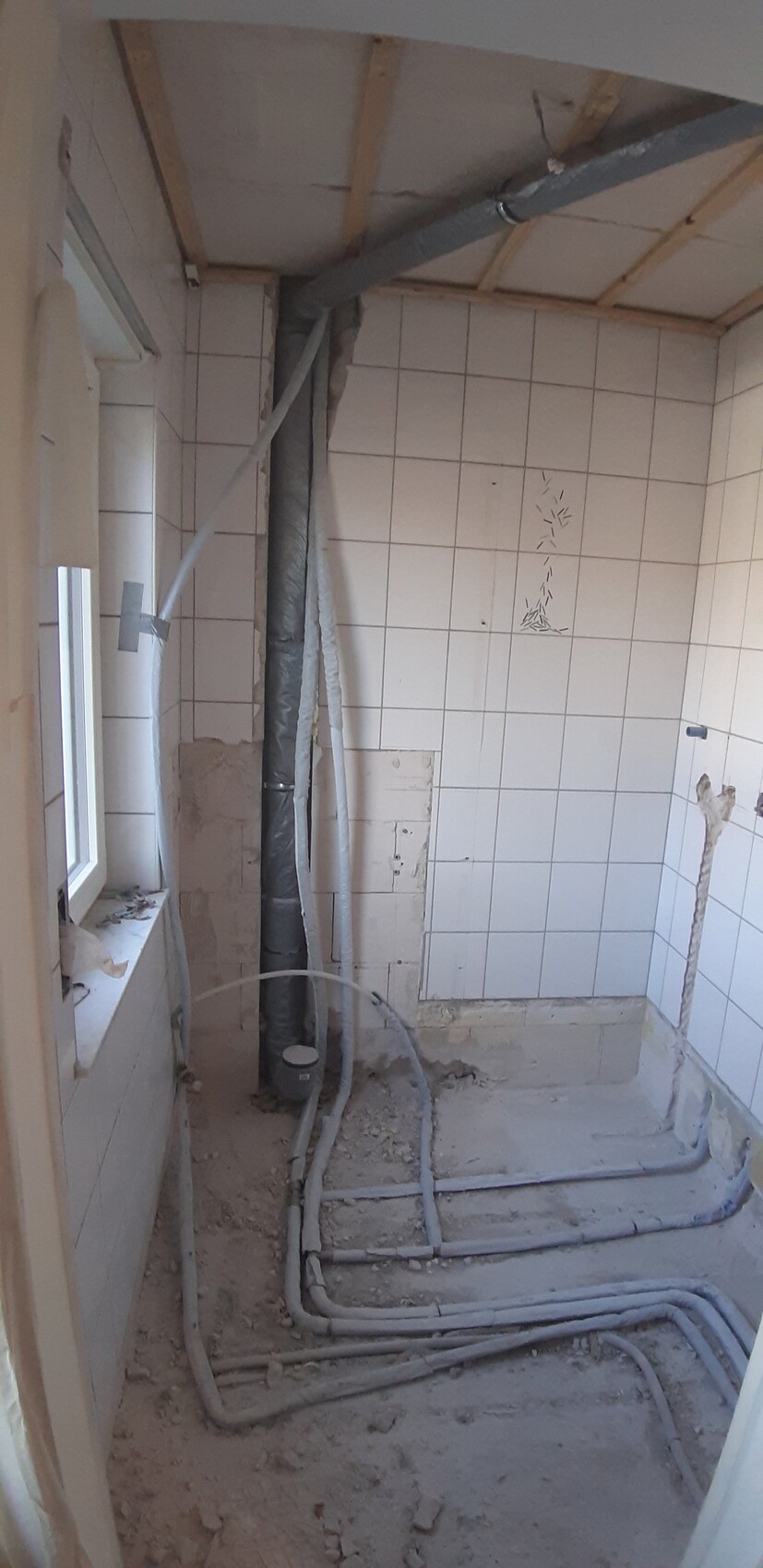 Badezimmer-Renovierung: freiliegende Rohre, weiße Fliesenwand, Staub und Kabel.