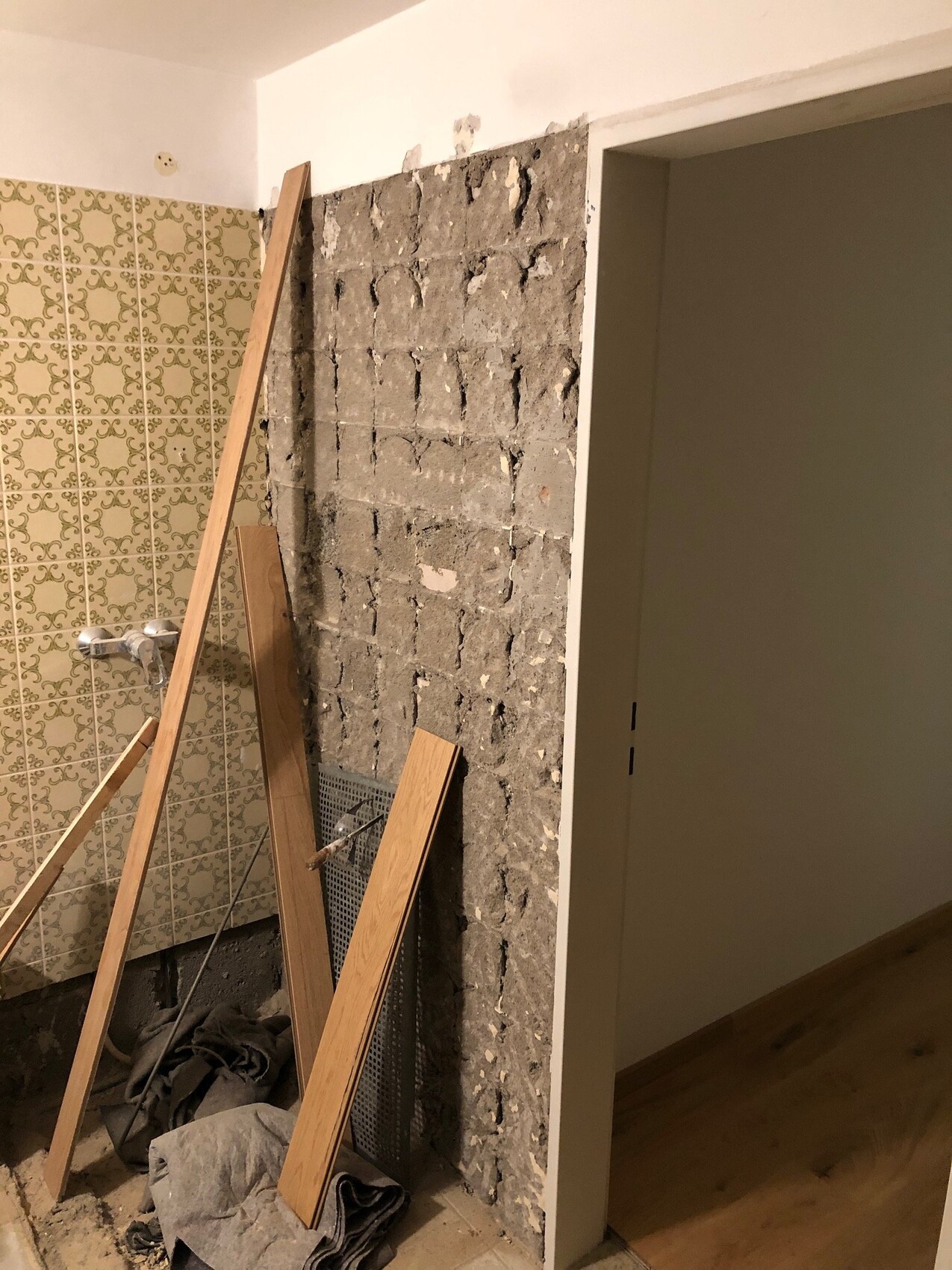 Baustelle im Badezimmer: freigelegte Betonwand, Holzlatten, linke Fliesenwand, Türrahmen rechts.