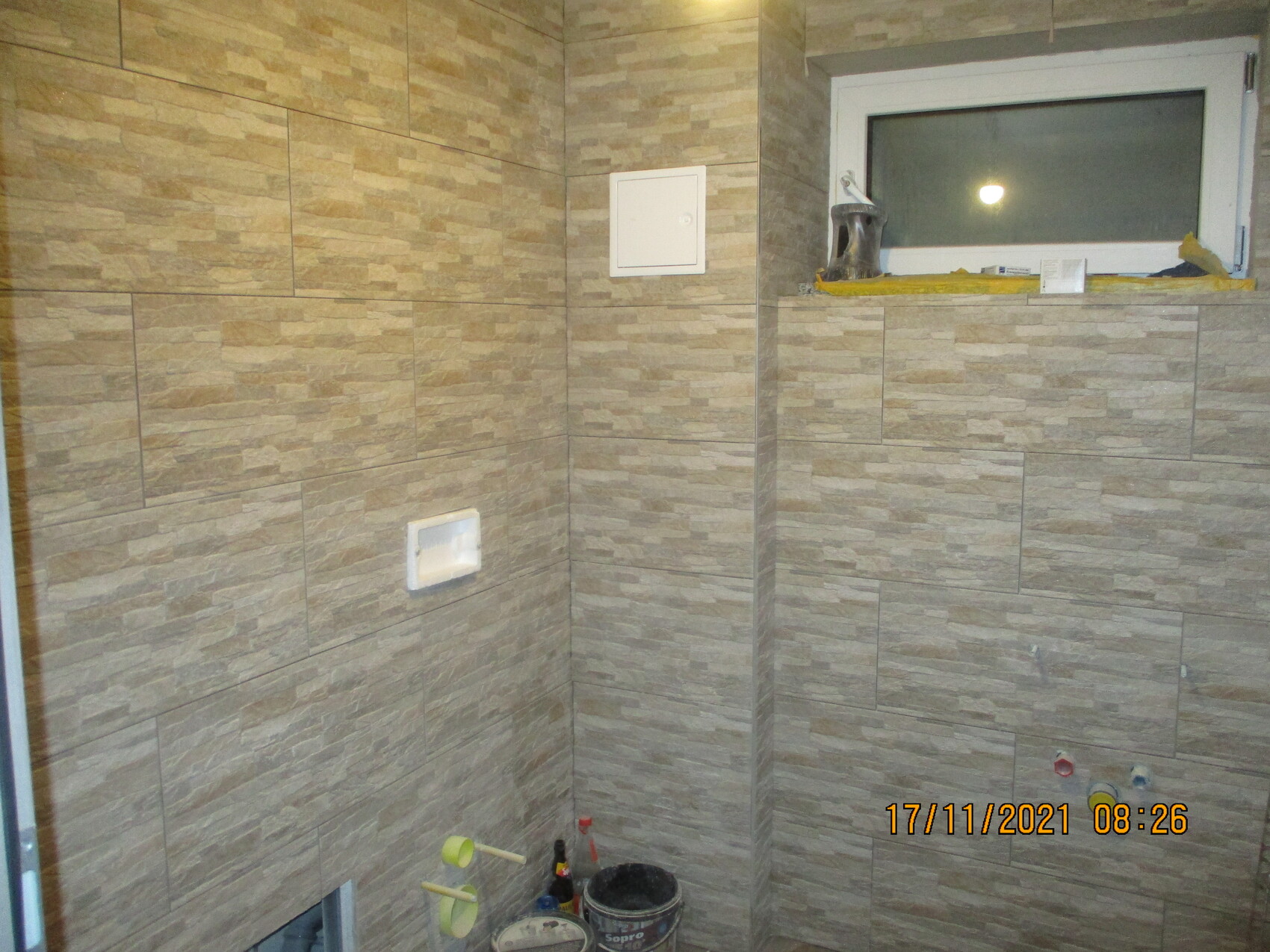 Badezimmer mit beige Steinfliesen, Fensterbank mit Werkzeugen und Bauutensilien.