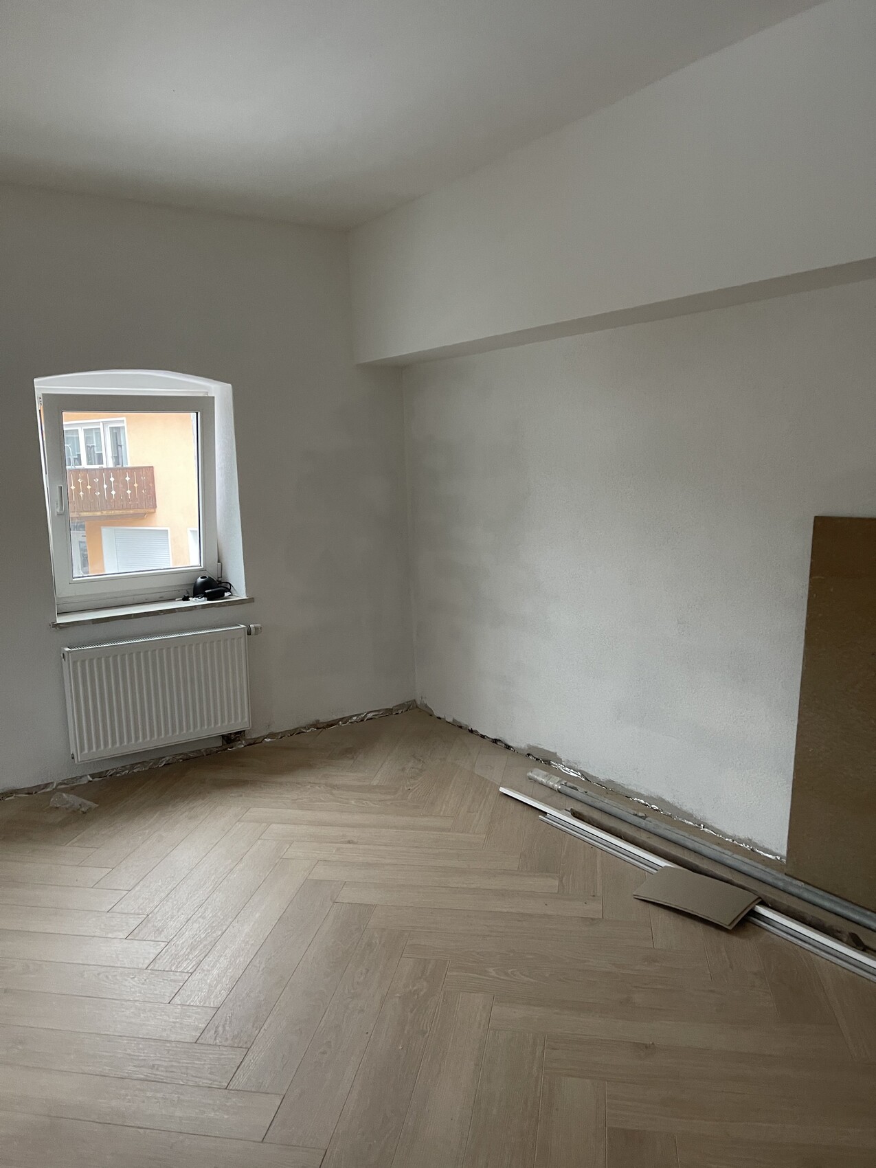 Leeres Zimmer in Renovierung mit Fenster, Heizkörper und Bauutensilien am Boden.
