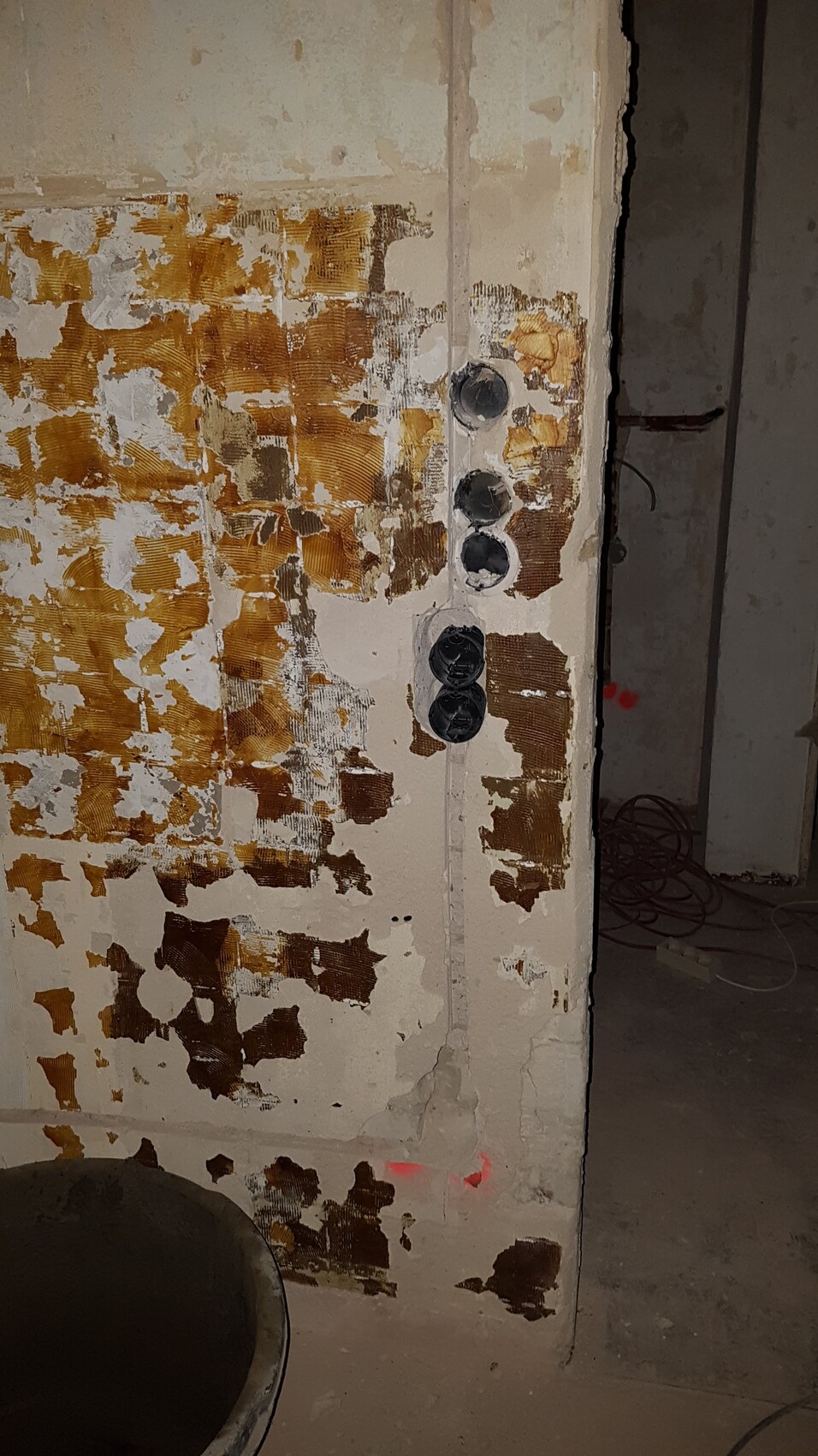 Wand mit abblätternder Tapete, braune Flecken; senkrechte Reihe aus fünf schwarzen Abdeckungen.