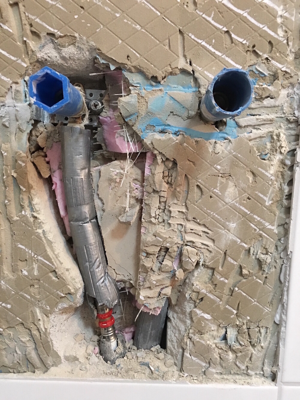 Ausgerissene Badezimmerwand mit Rohren, Dämmung und Installationen sichtbar.