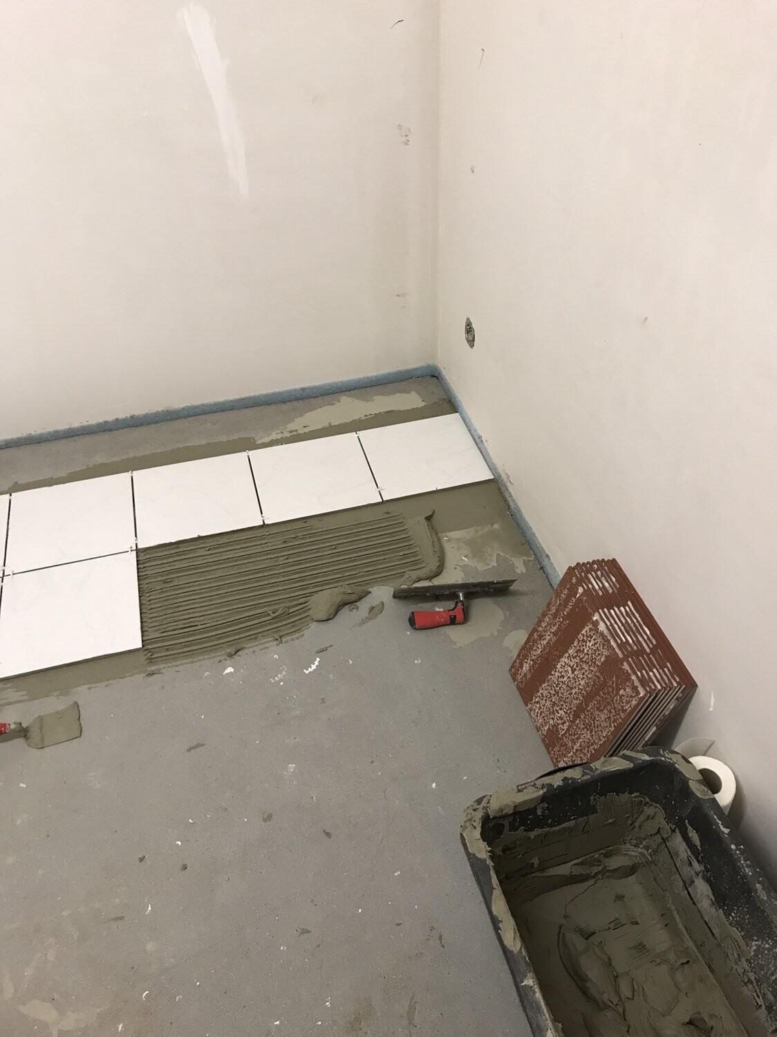 Badezimmer im Bau: weiße Quadratfliesen werden auf Kleber verlegt, Werkzeug.