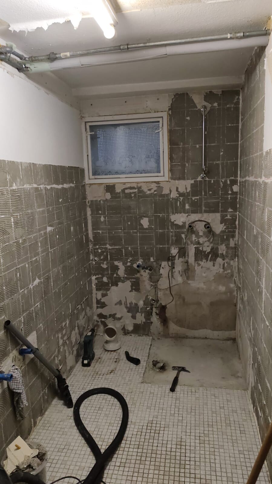 Kleines Badezimmer während Renovierung mit freiliegenden Fliesen, Rohren und Werkzeugen