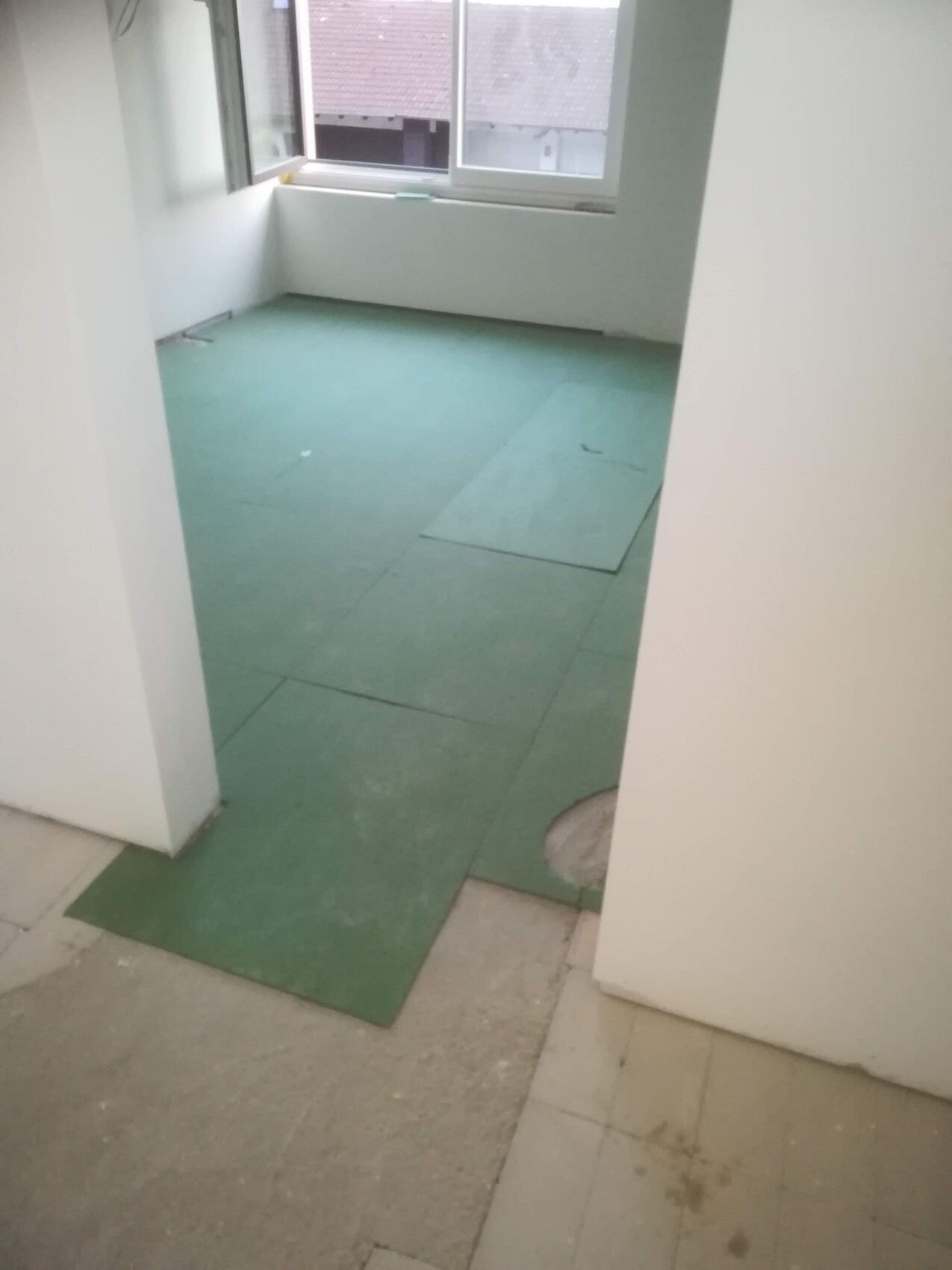 Kleiner renovierter Raum mit grünem Bodenbelag aus Platten, geöffnetem Fenster und Loch im Boden
