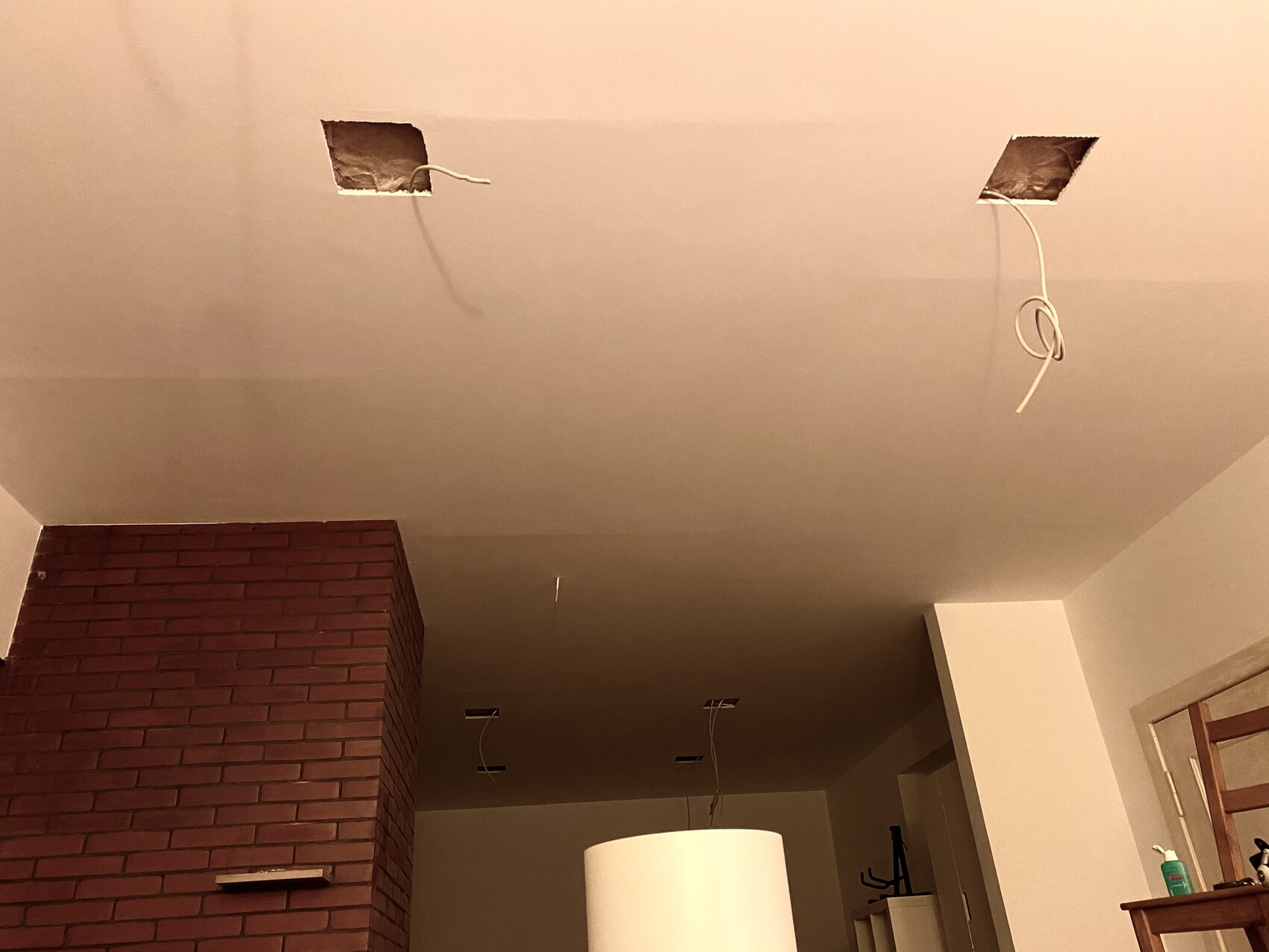 Decke mit offenen Kabelauslässen und losen Kabeln; rote Ziegelwand links, weißer Lampenschirm unten.