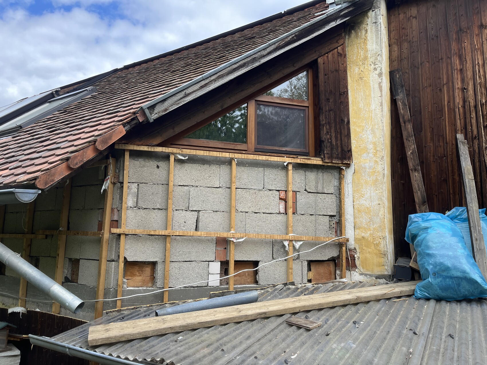 Aussenansicht eines renovierungsbeduerftigen Hauses mit unfertiger Wand, Holzrahmen und Dachziegeln