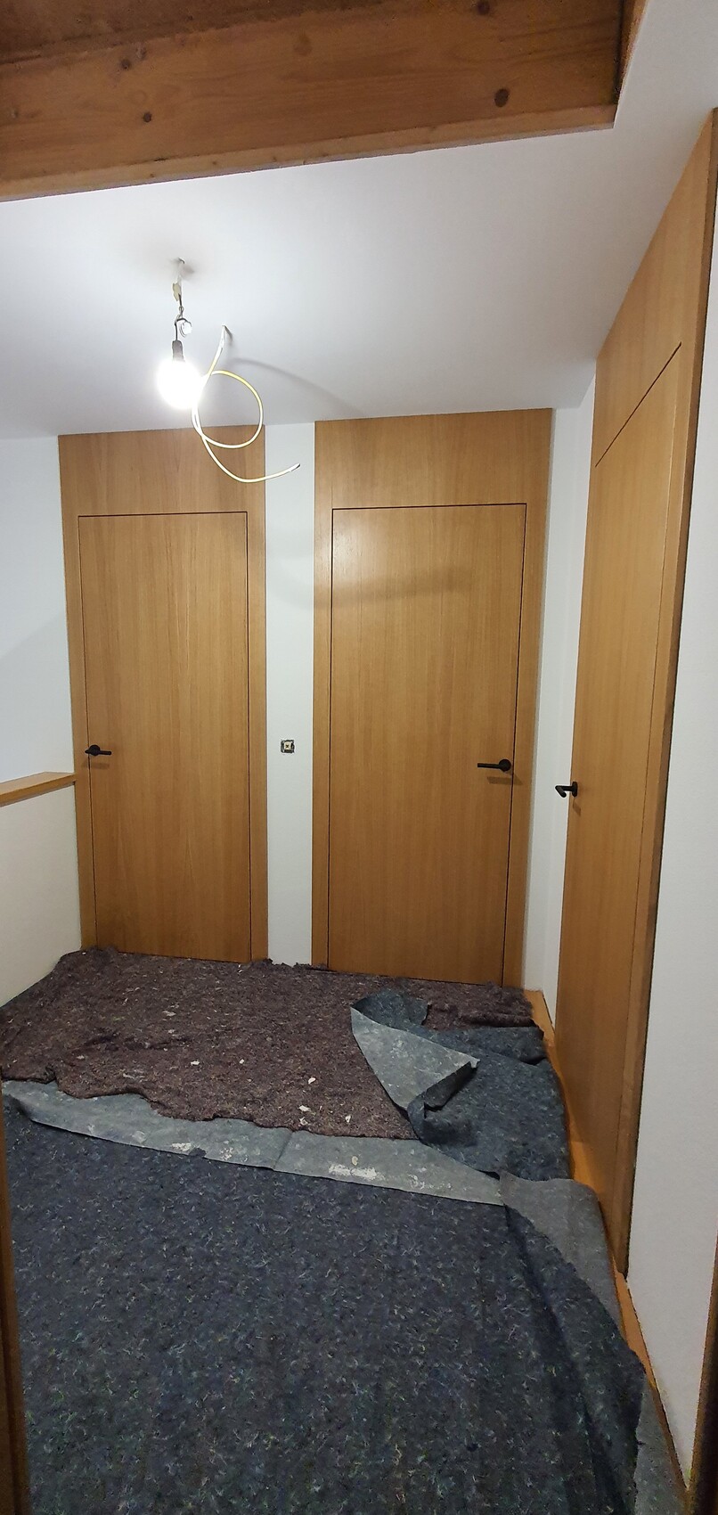 Flur mit drei Holztüren, offener Deckenbalken, provisorische Beleuchtung.