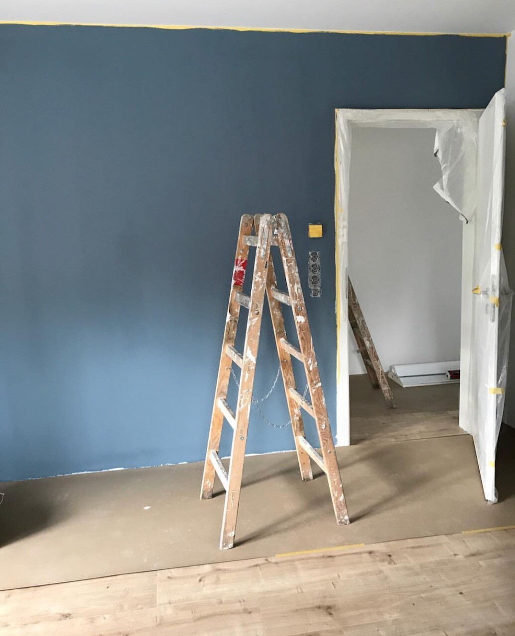 Blaue Wand im Renovierungsraum, Holzleiter vor Türrahmen mit Abdeckfolie.