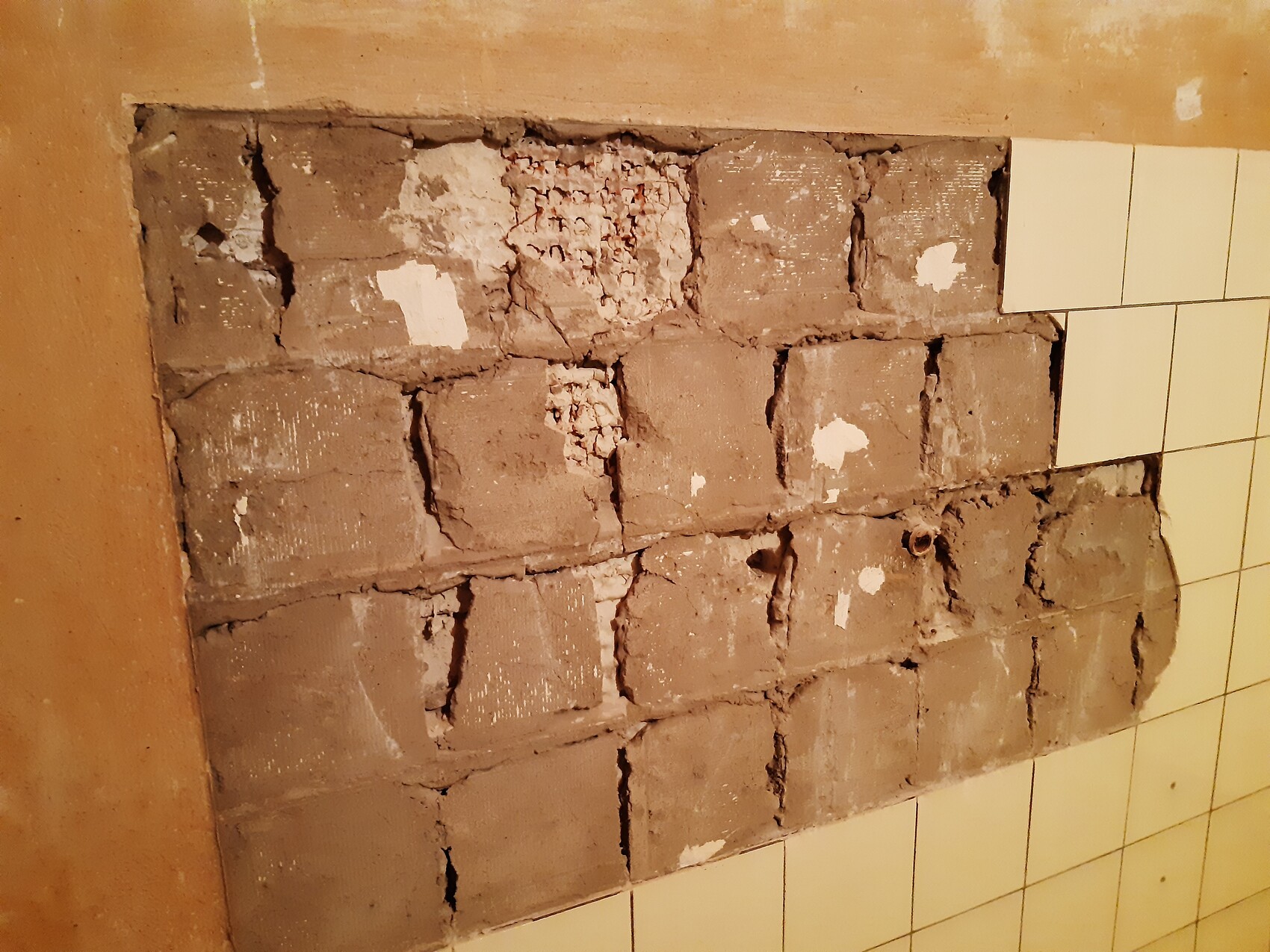 Freigelegte Wand aus Ziegel-/Betonblöcken mit brüchigem Putz, daneben Fliesen.