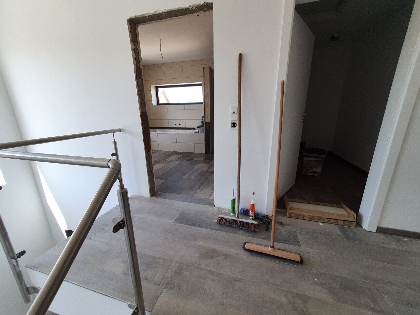 Renovierter Flur mit Metallgeländer, Besen, Reinigungsmittel; Durchgang zum Badezimmer.