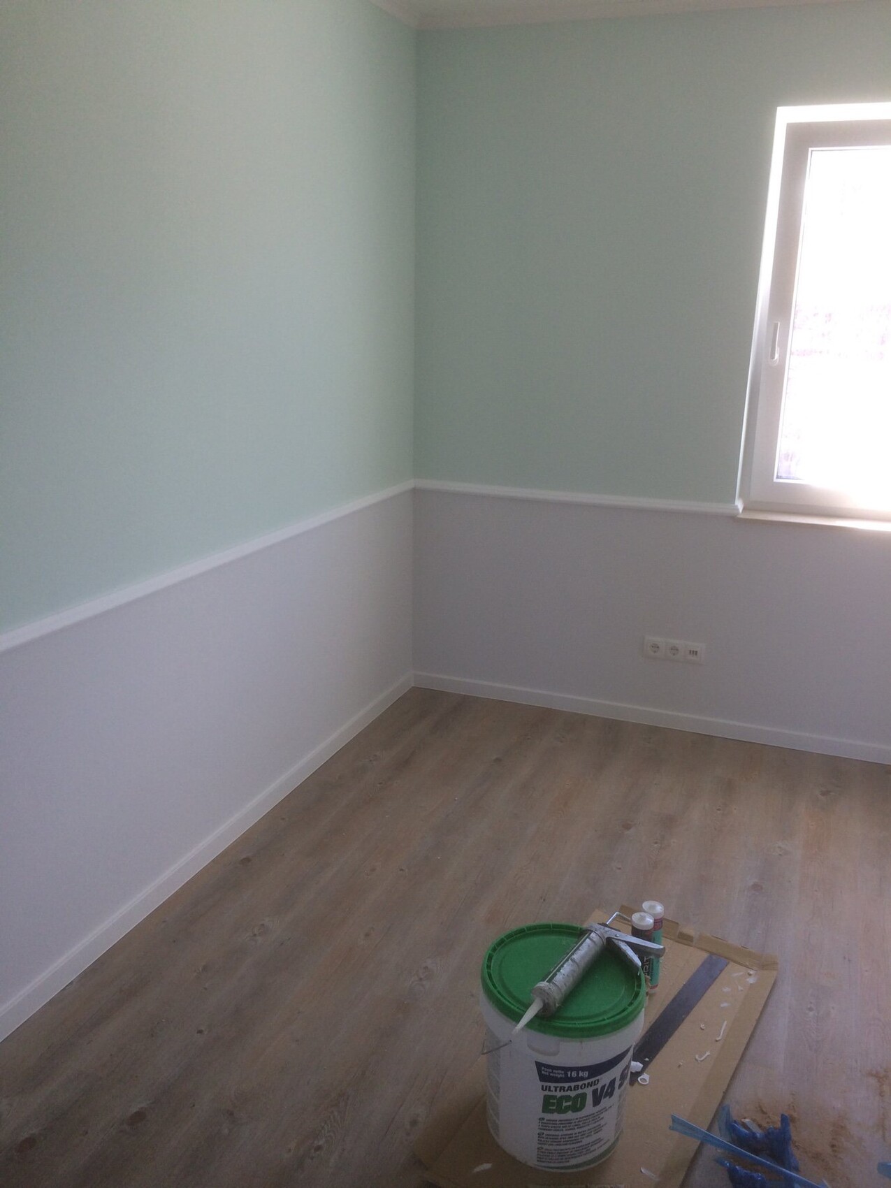 Renoviertes Zimmer mit mintgruenen Wänden, Holzboden und Malerwerkzeug.