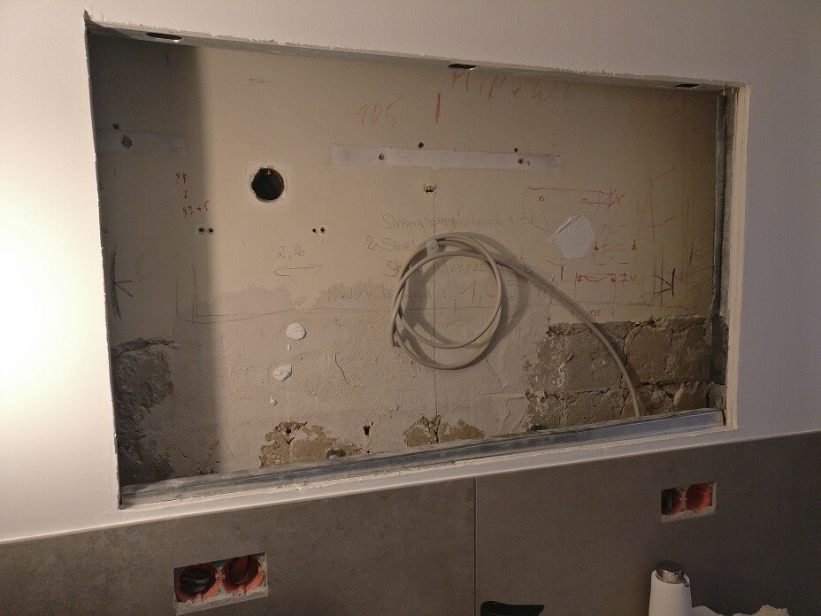Offene Wandöffnung mit losem Kabel, Putz- und Betonresten im Innenbereich.