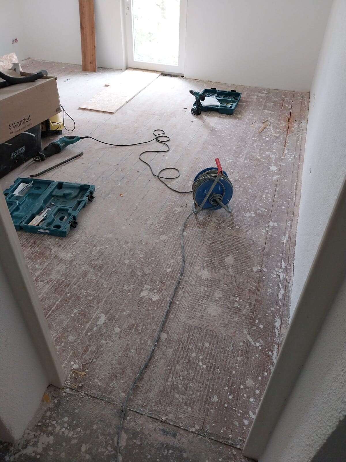 Renovierungsraum mit Bohrmaschine, Kabeltrommel, Werkzeugkisten und Holzdielenboden.