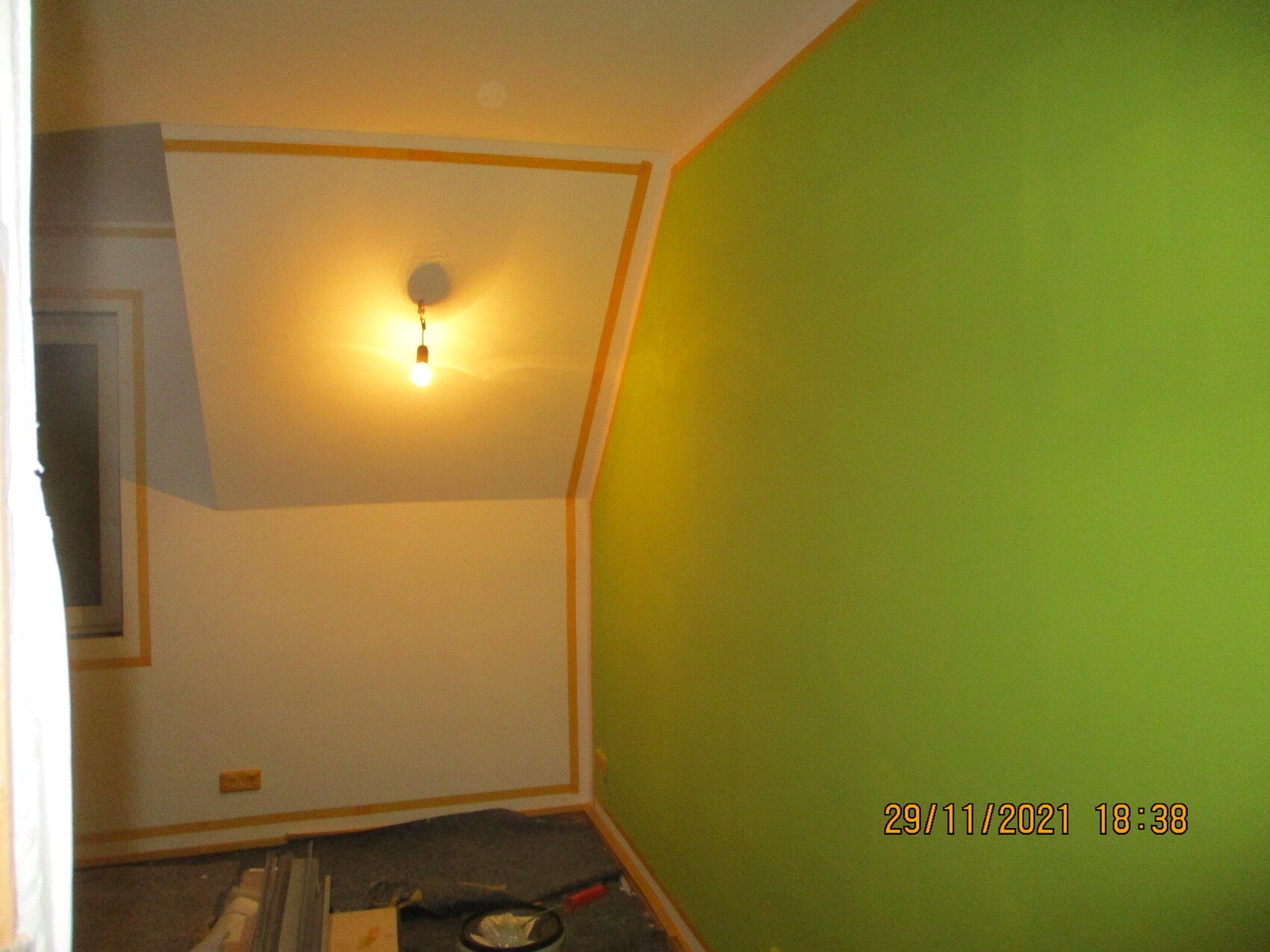 Renovierungsraum: grüne Wand rechts, weiße Decke mit Malerklebeband, hängende Glühbirne.