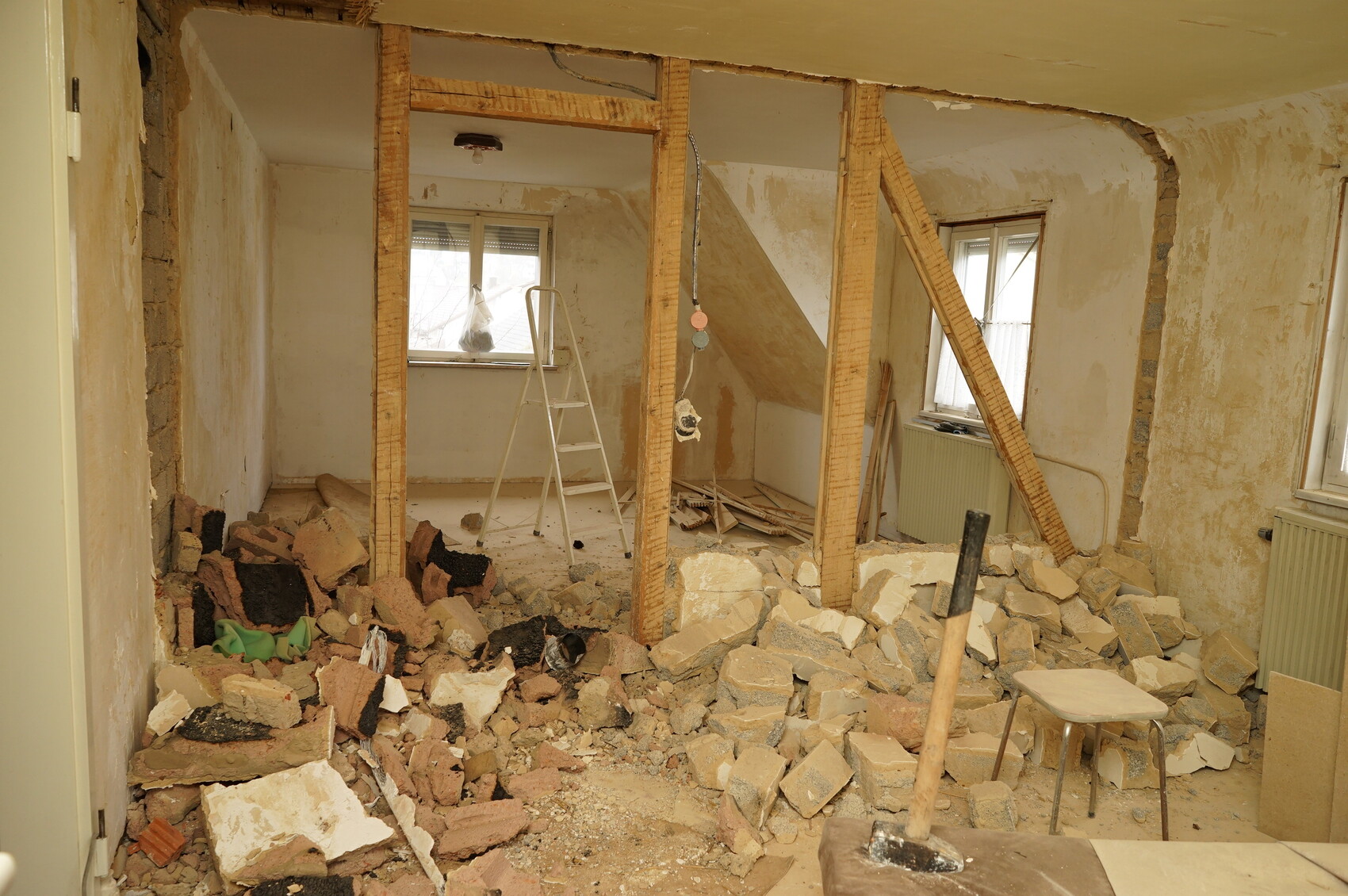 Raum im Umbau: Ziegel- und Steinmüll, freigelegte Holzbalken, Leiter und Bauwerkzeuge.