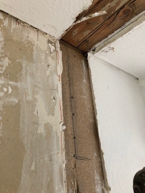 Renovierungsbereich: Ecke mit sichtbarem Holzbalken an der Decke, unverputzter Wand und Nägel.