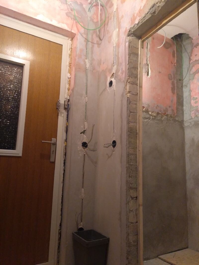Flur/Renovierungsraum mit freiliegten Kabeln, Rohbauwand und Eimer neben Tür.