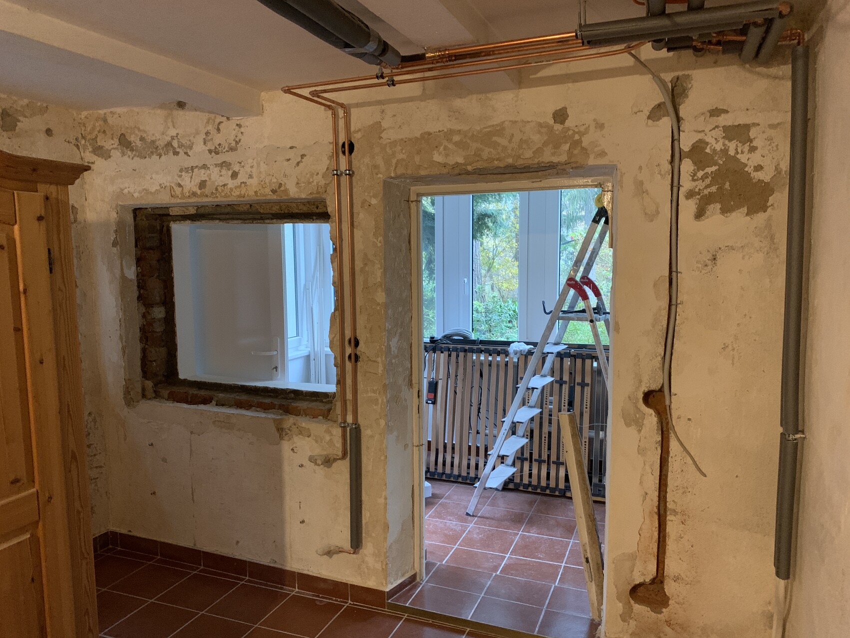 Renovierungsraum mit freigelegten Wänden, Rohren und einer Leiter vor Fensteröffnung.