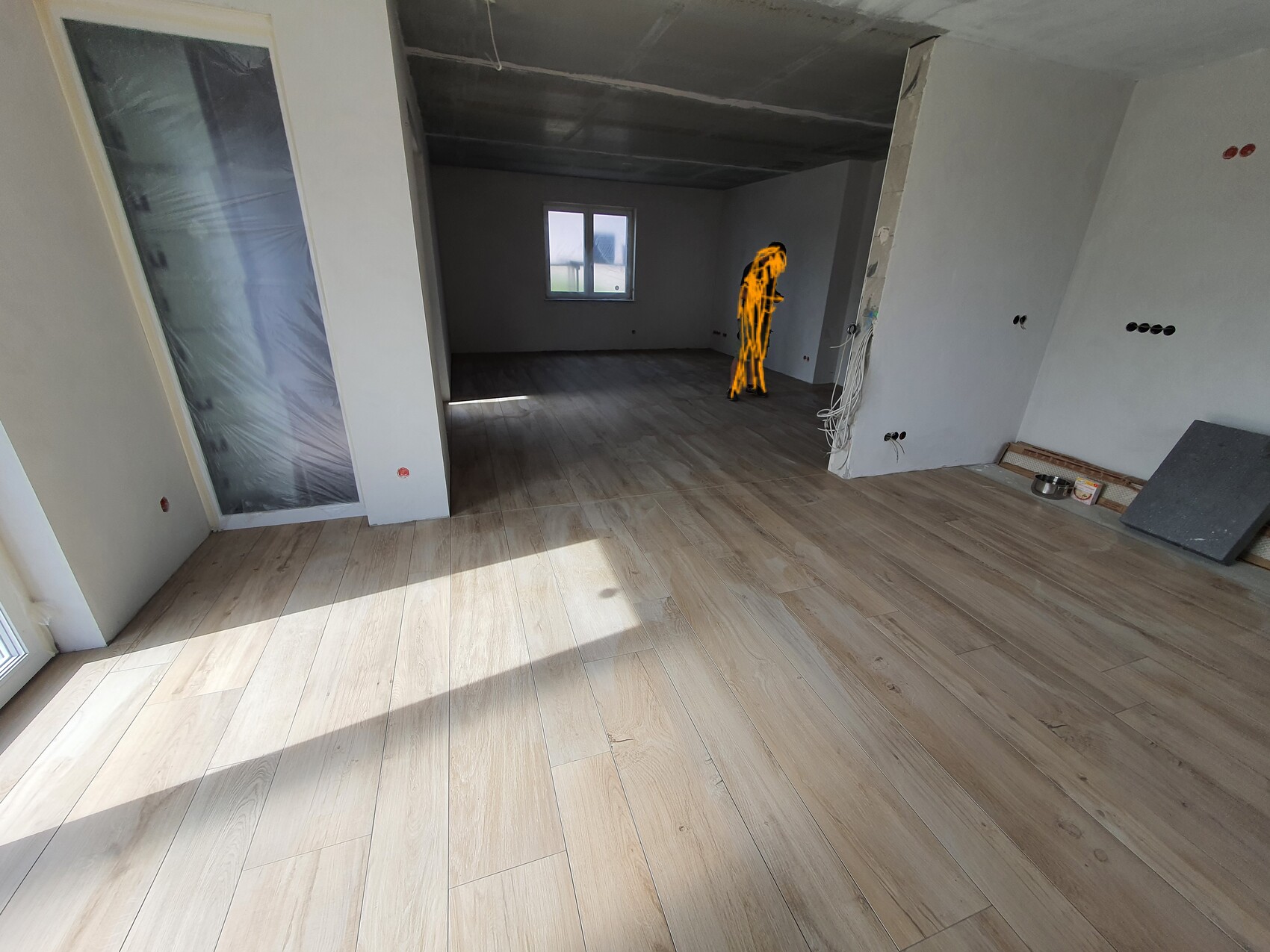 Renovierungsbereich: heller Raum mit Holzboden, Kabeln, orange markierte Person bei Arbeiten