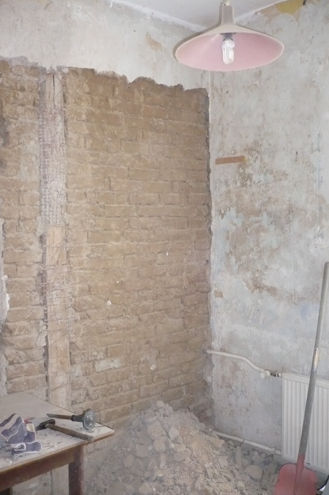 Renovierungsraum: freiliegende Backsteinwand, Putzbruch, Schutt, Tisch mit Werkzeug, rosa Lampe