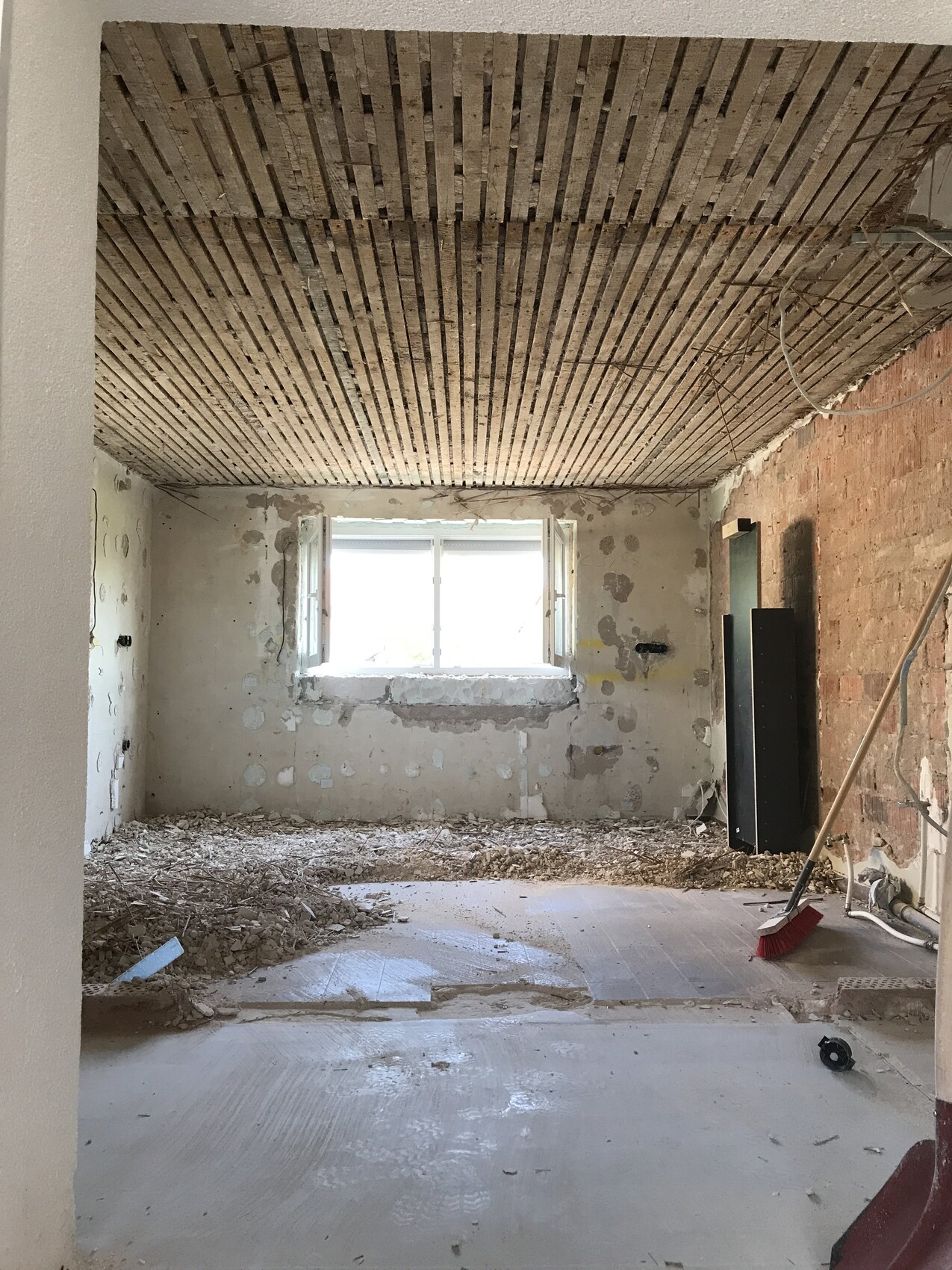 Renovierungsraum mit freigelegter Decke aus Latten, verputzten Wänden, Staub und Besen.
