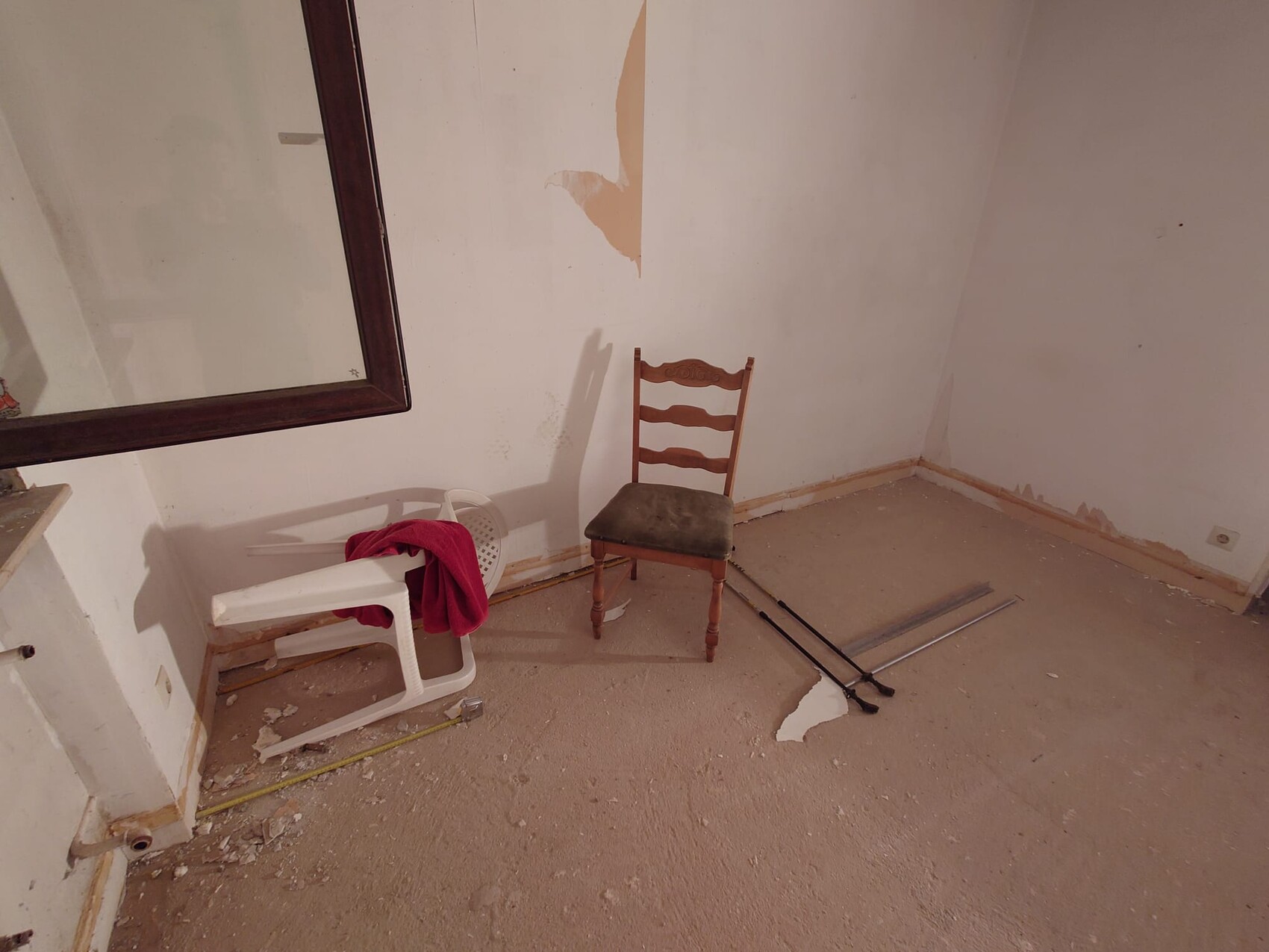 Innenraum mit beschädigter Wand, altem Holzstuhl und Bauabfall während Renovierung