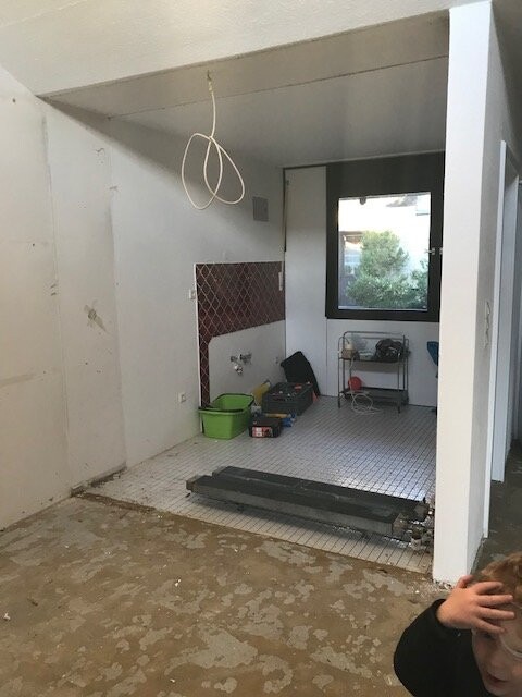 Küche im Rohbau mit Fliesenboden, Baumaterialien und offener Decke während der Renovierung