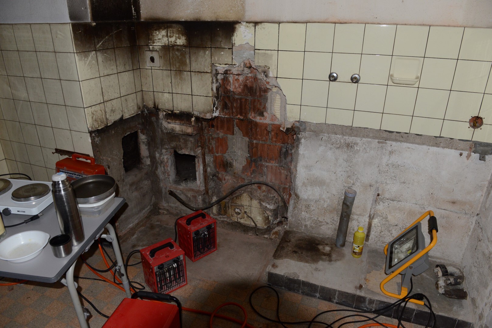 Küchenbereich mit beschädigter Wand, Fliesen, Rohren und Renovierungswerkzeugen.
