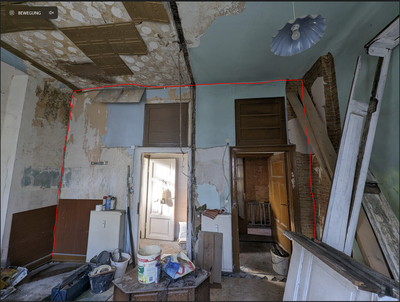 Verlassenes Innenraumzimmer: abblätternde Wände, Bauholz, Eimer, Werkzeug und Müll.