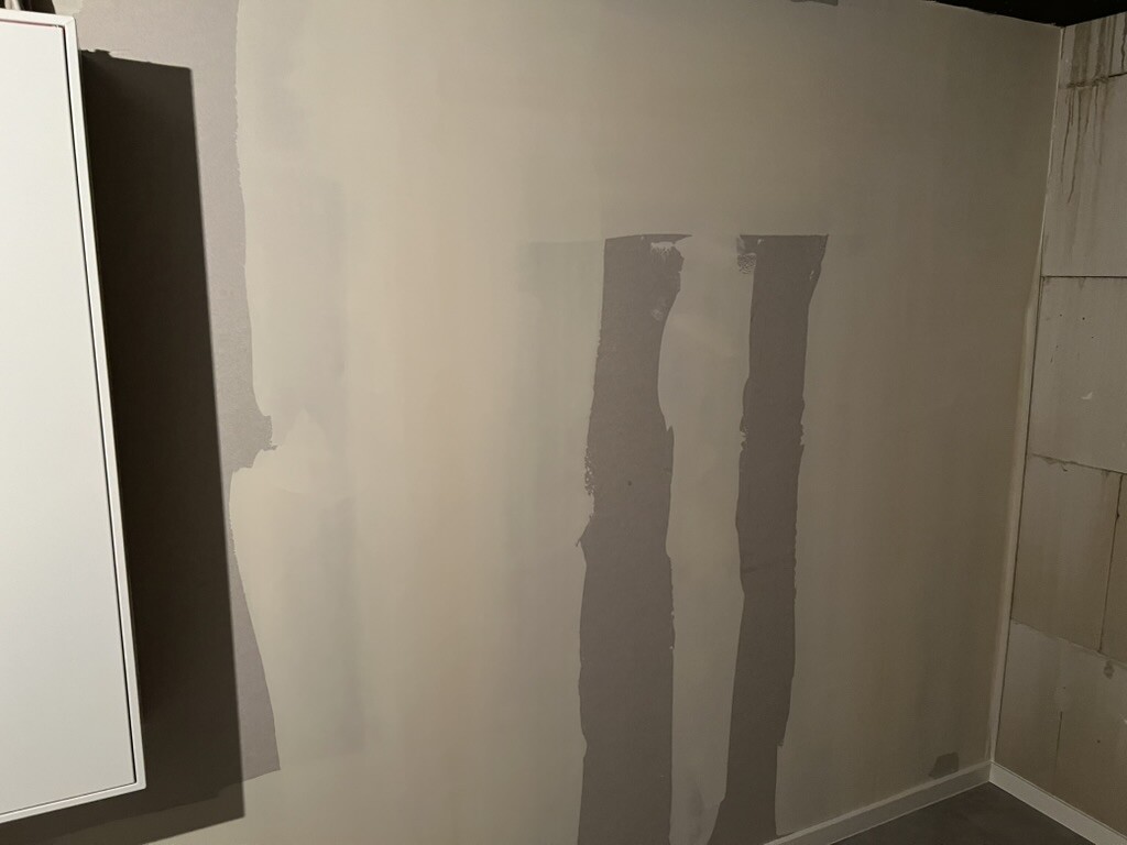 Wand mit mehreren vertikalen Spachtelstreifen; links Schrank, rechts Fliesen.