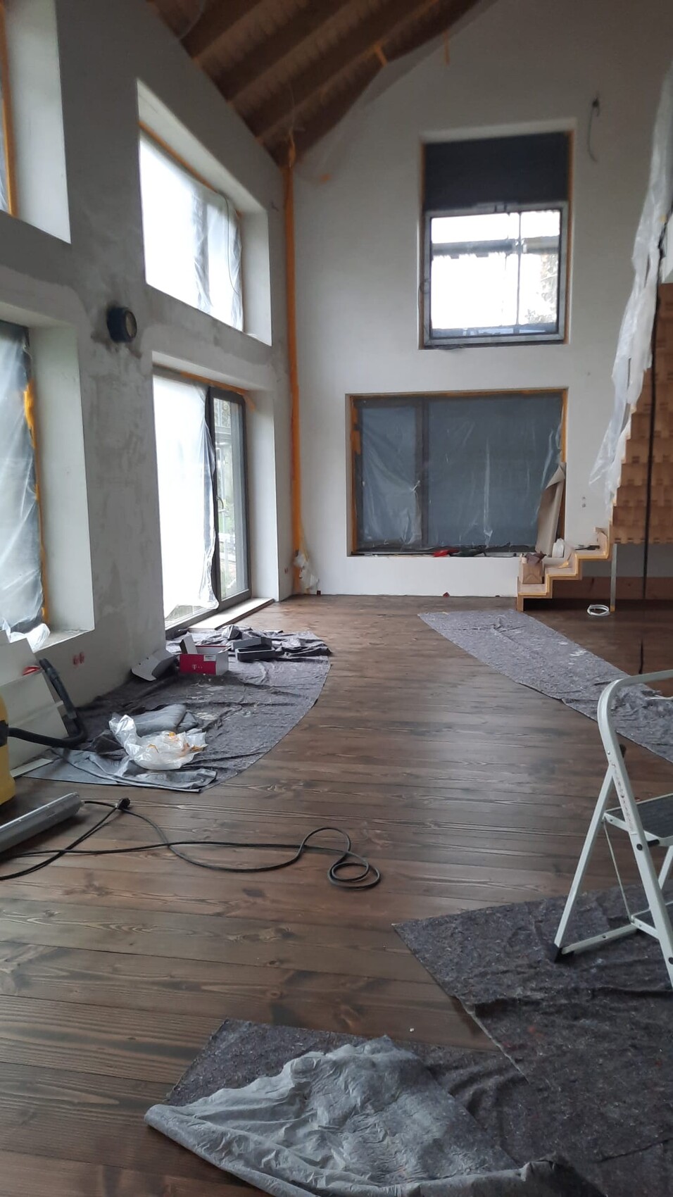 Heller offener Rohbau-Raum mit Holzfußboden, großen Fenstern, Abdeckplanen und Werkzeugen.