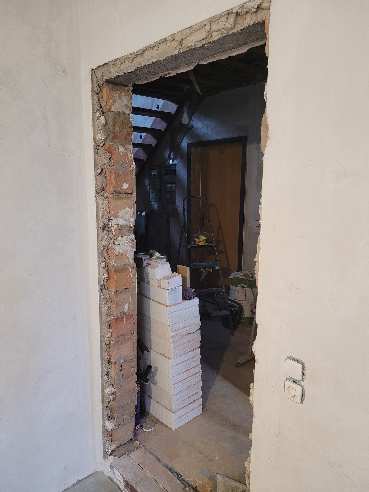 Renovierungsraum durch offenen Wanddurchbruch: Ziegelrahmen, Treppe, Tür und Styroporblöcke.