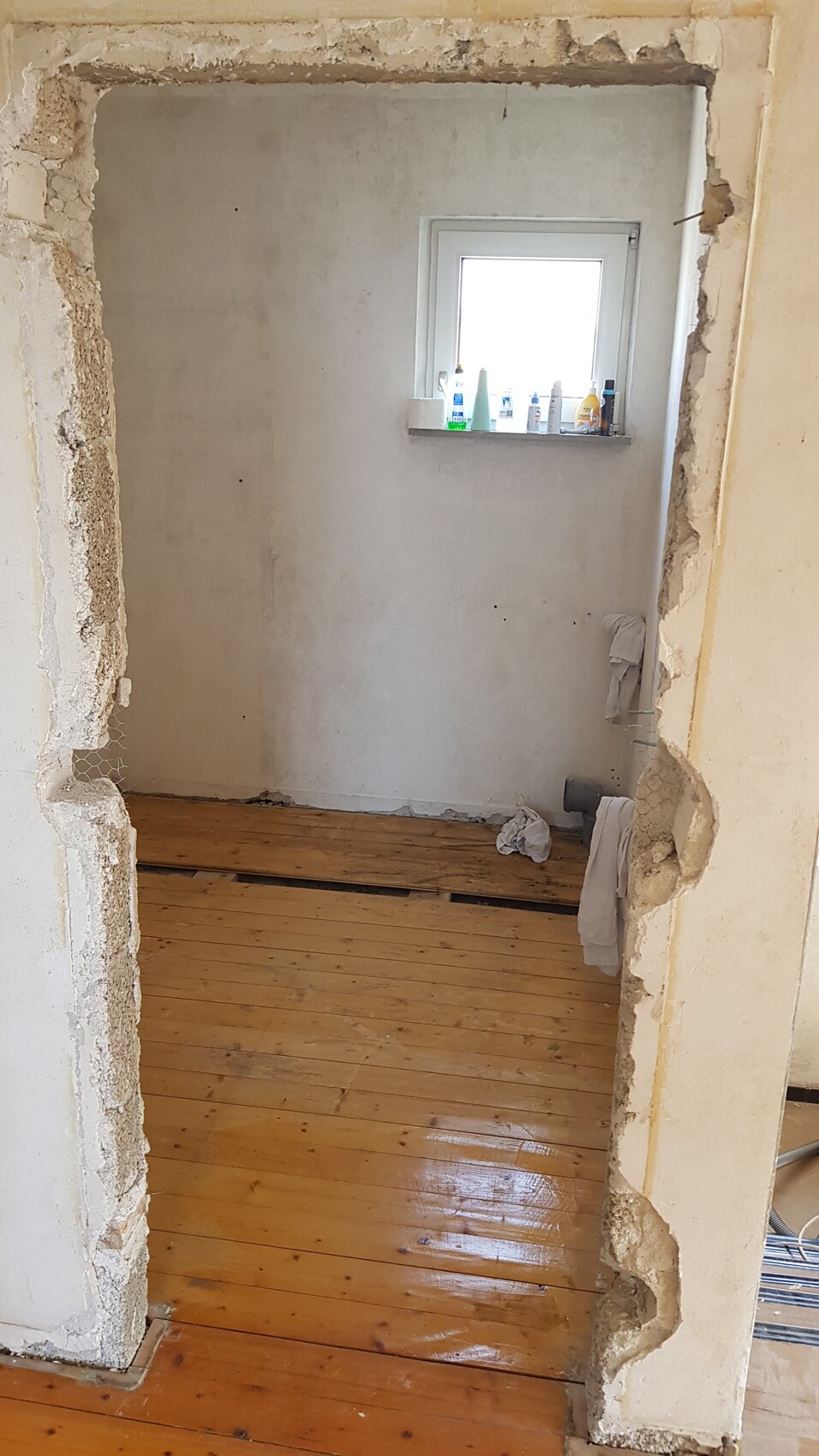 Rohbauraum mit offenem Wanddurchbruch, Holzfußboden und Fensterbank mit Reinigungsmitteln