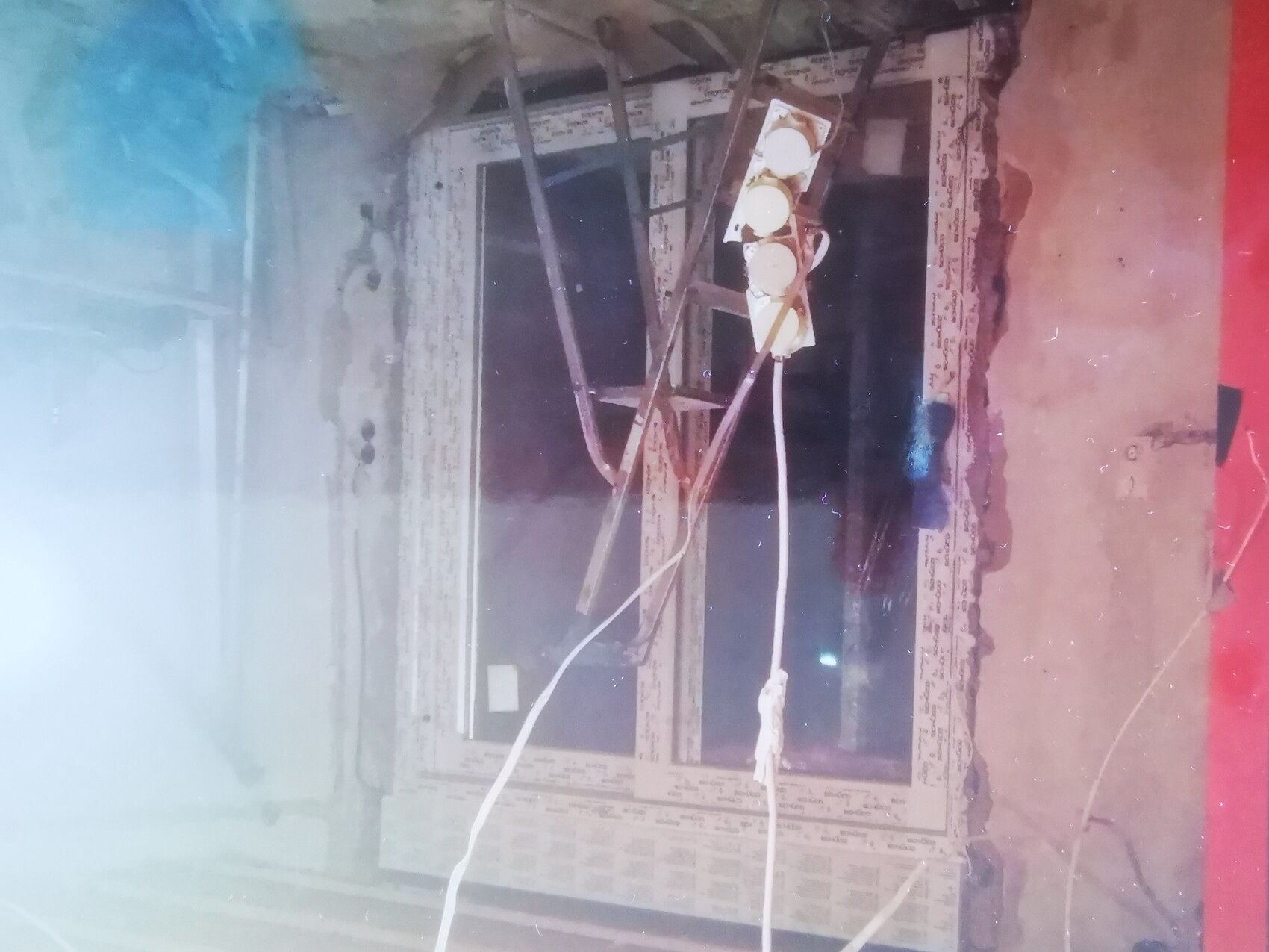 Verwitterte Wand mit Fensterrahmen, lose Kabel und Mehrfachstecker.