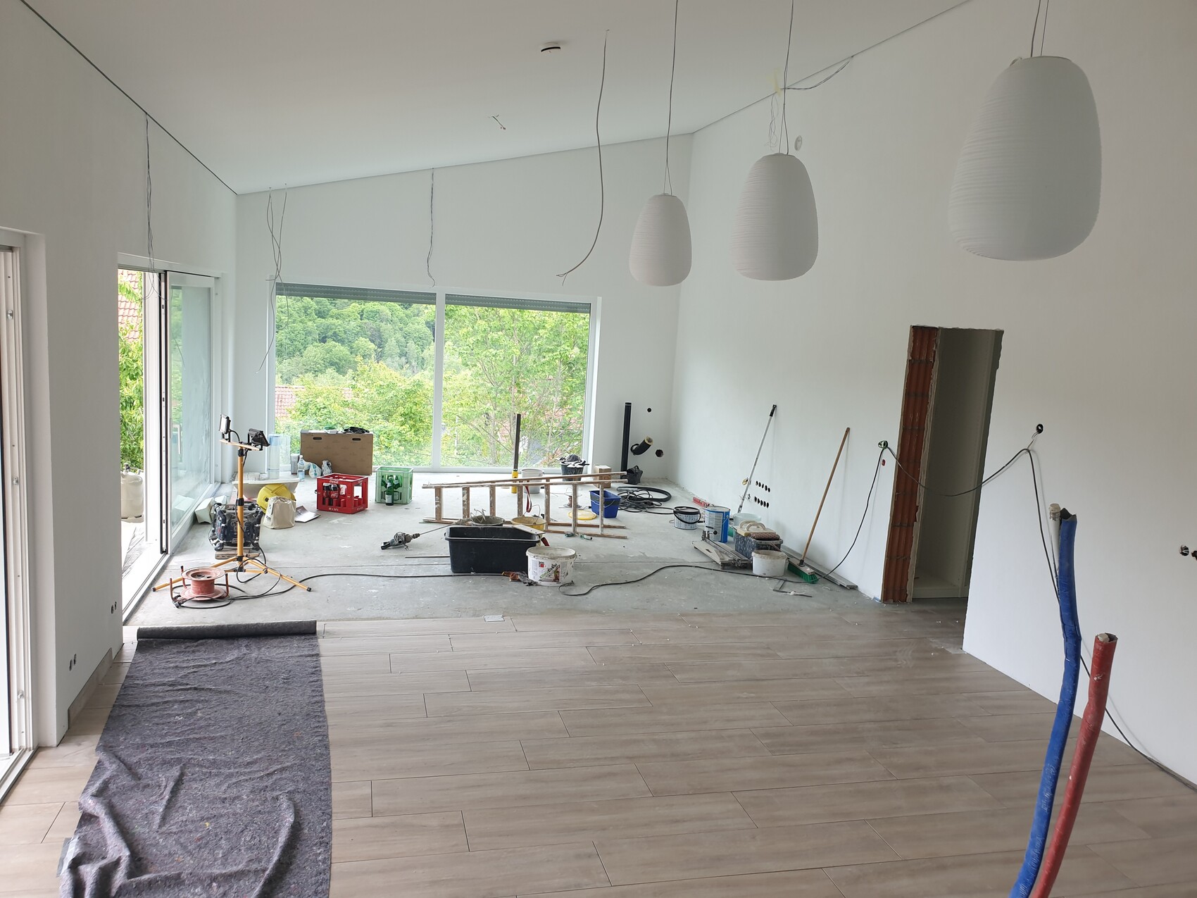 Heller Renovierungsraum mit weißen Hängeleuchten, Bauwerkzeugen und großen Fenstern mit Gartenblick