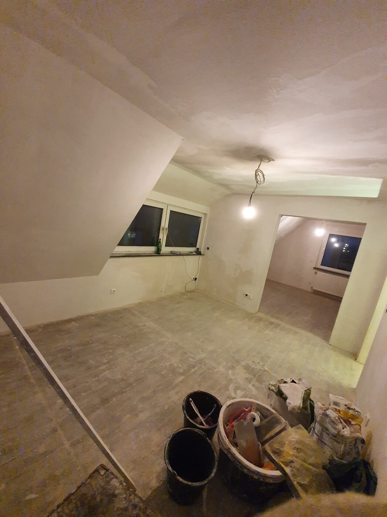 Unrenovierter Innenraum: freiliegende Decke, Bauutensilien in Eimern, Hängelampe, Fenster.