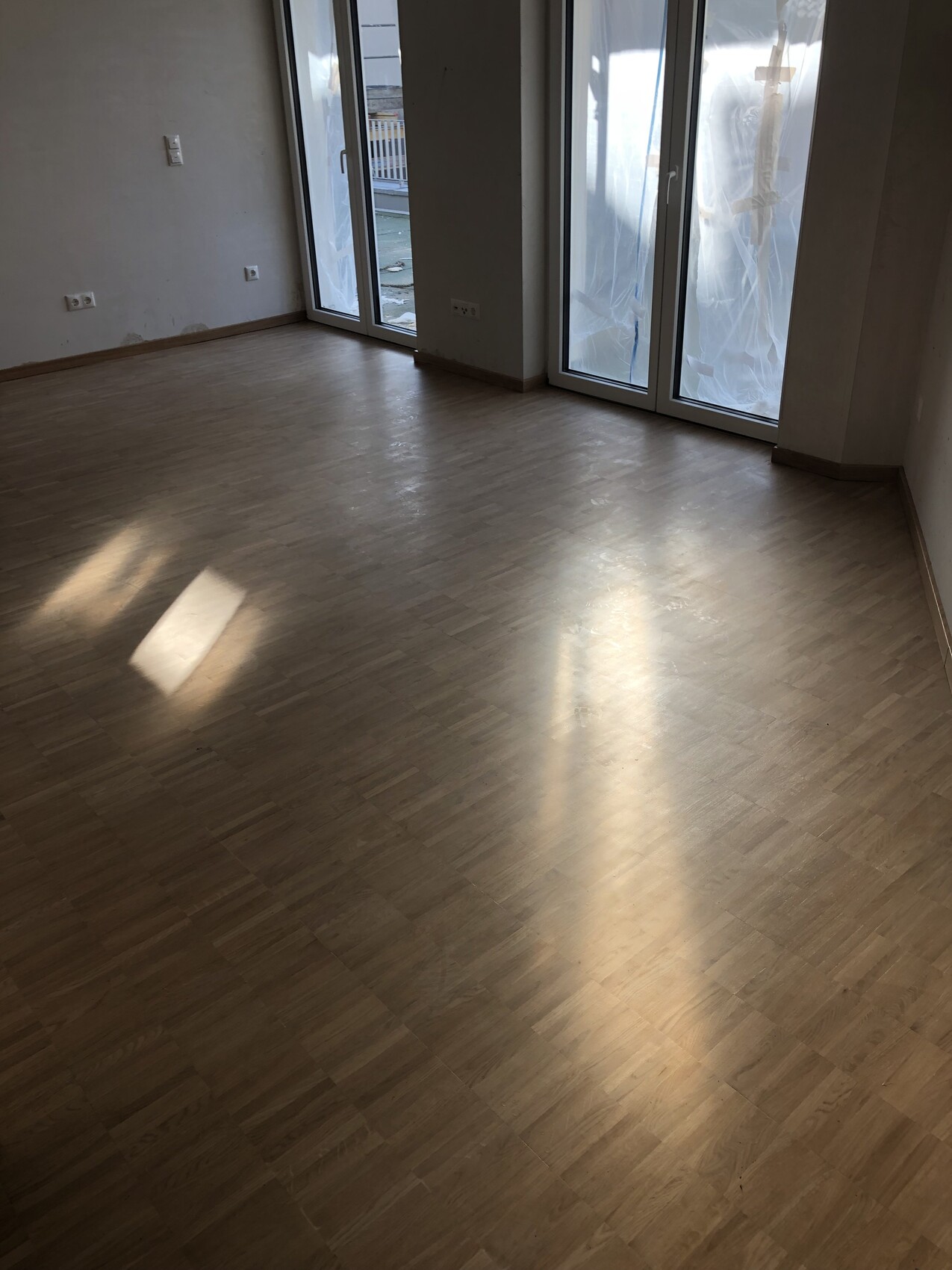 Leerer Raum mit Holzfußboden und großen Fenstern, Sonnenlicht reflektiert auf dem Boden