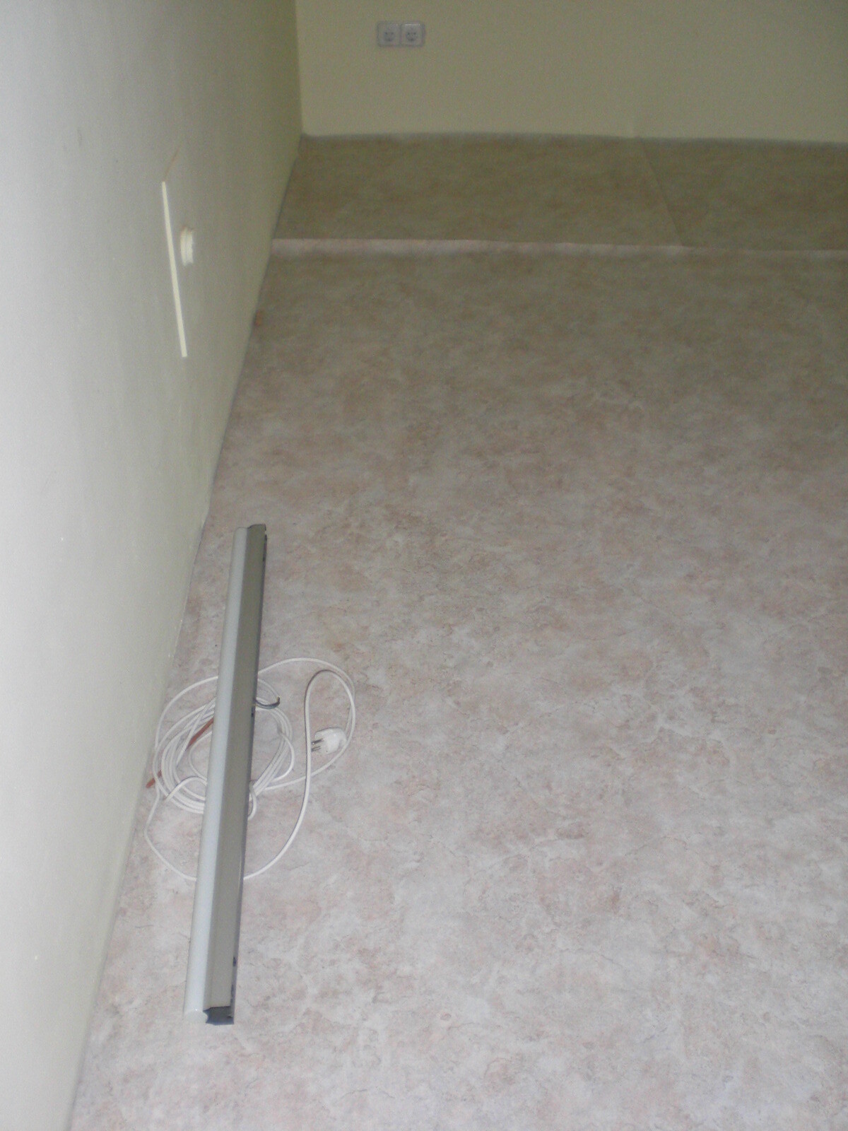 Unbearbeiteter Innenraumboden mit losem Kabel und Wandanschlüssen, Renovierungszustand.