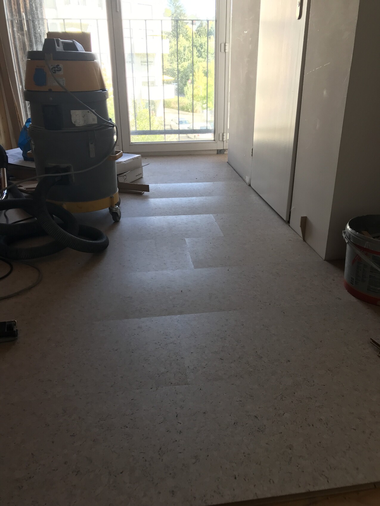 Renovierungsraum mit Staubsauger, Schlauch, Eimer und Balkon-Tür im Hintergrund.