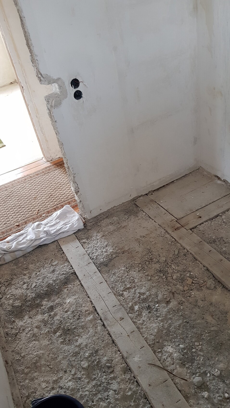 Renovierungsraum: Boden mit Brettern, Staub, Wand mit zwei runden Öffnungen, weißes Tuch auf Boden