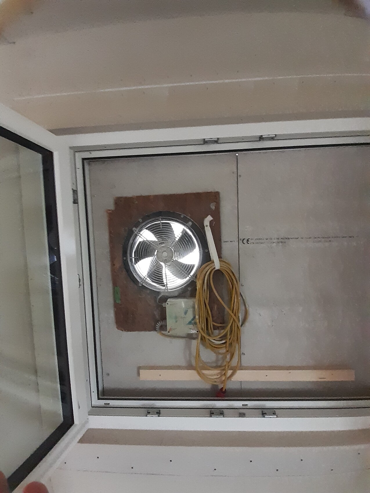 Runder Ventilator an brauner Wandplatte, gelbes Kabel aufgewickelt.